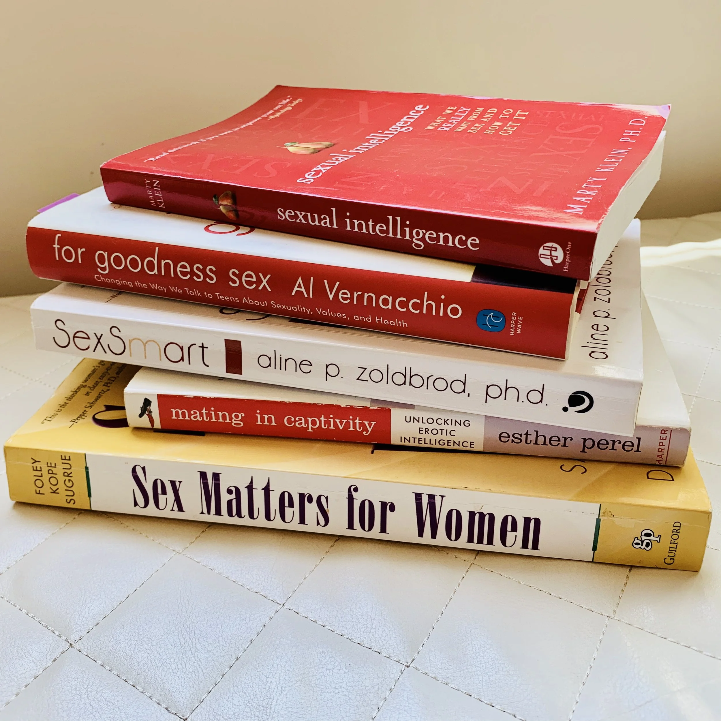 Stacked books on sexuality, including titles such as "Sexual Intelligence," "For Goodness Sex," and "Sex Matters for Women," placed on a tiled surface.