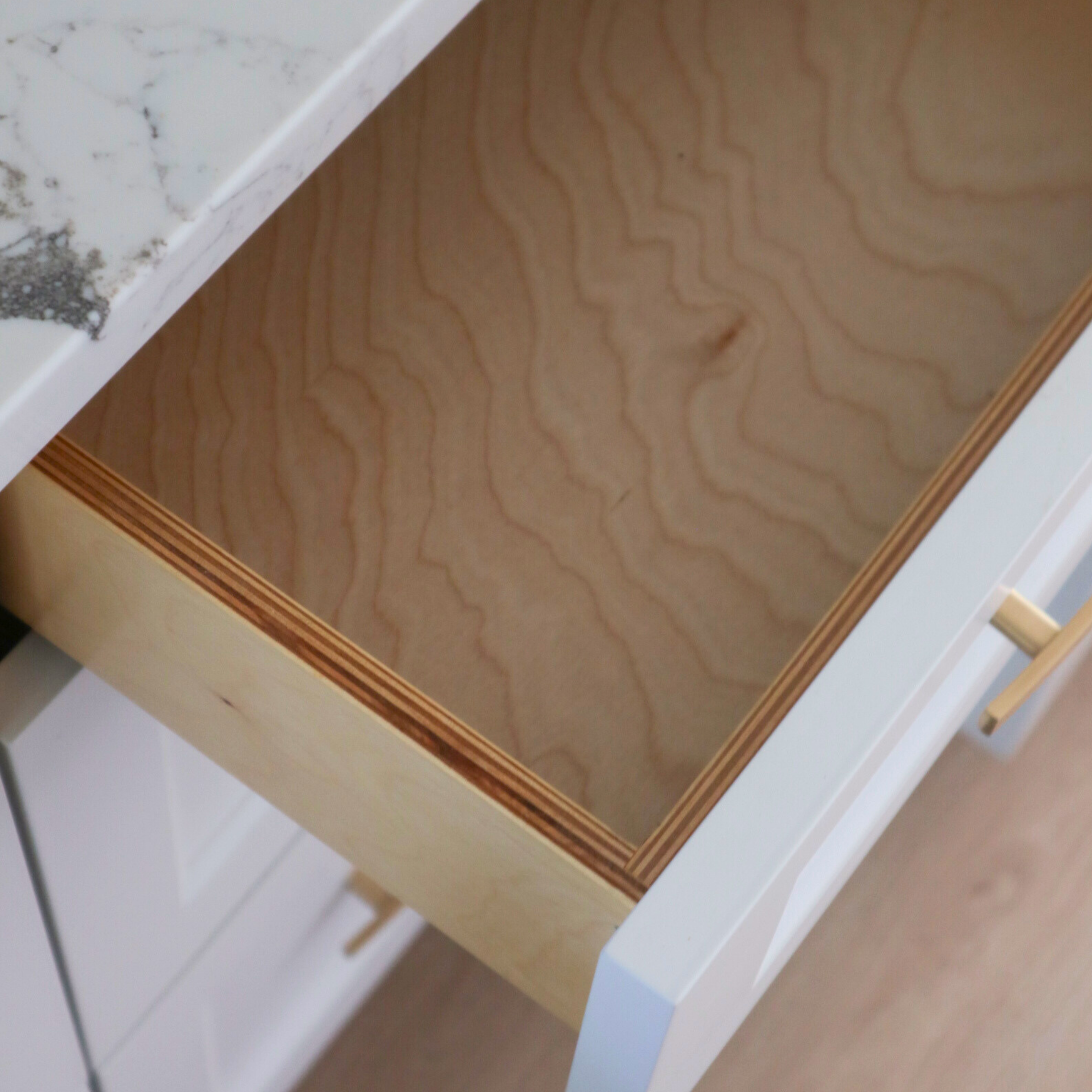 Open wooden drawer inside a white cabinet, with a visible wood grain interior.