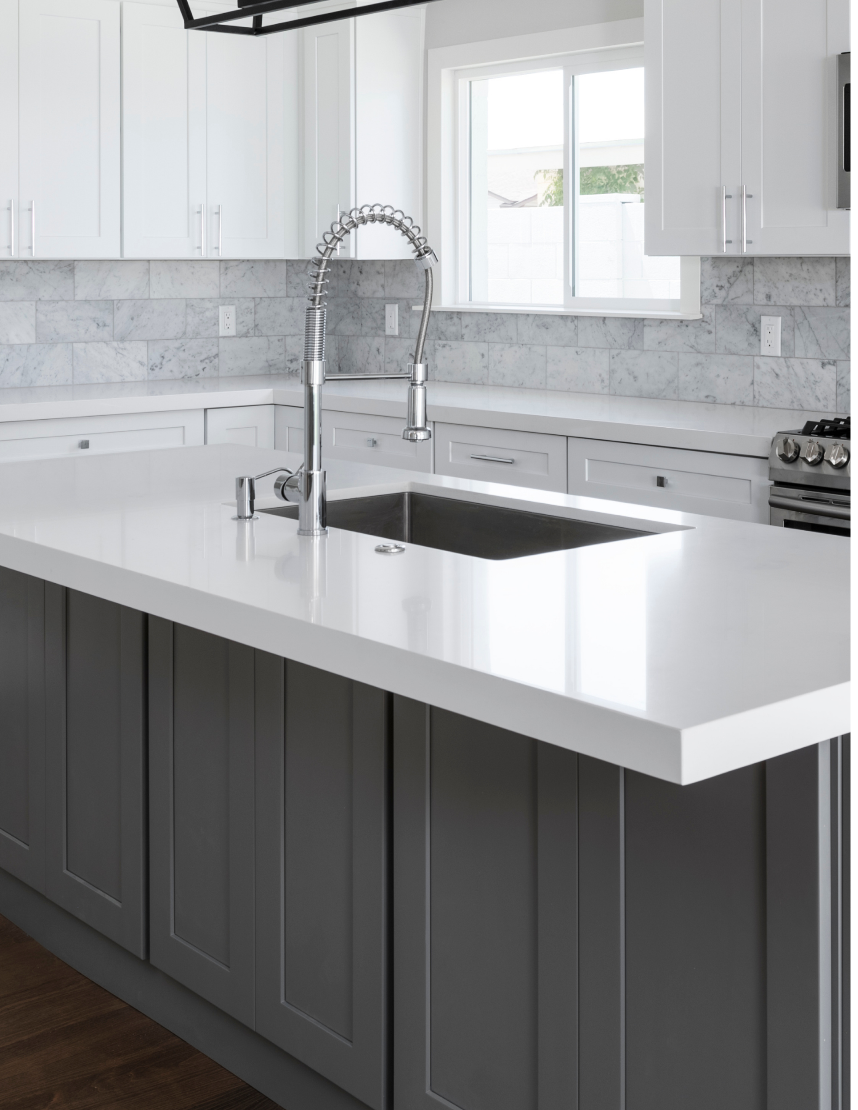 Modern kitchen with white cabinets, a gray island with a white countertop, a black sink, a spring faucet, a window, and stainless steel appliances.