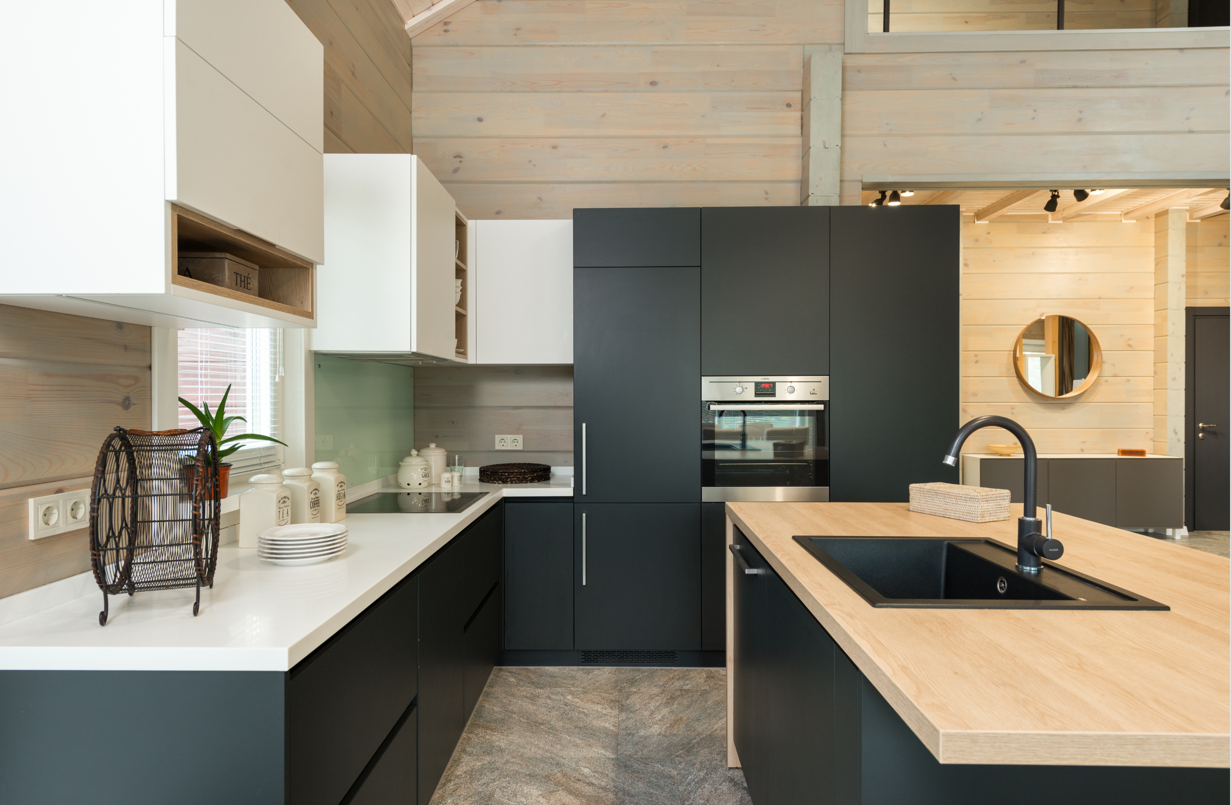 Modern kitchen with black and white cabinets, wooden countertops, a black sink, and a built-in oven, with wooden walls and ceiling.