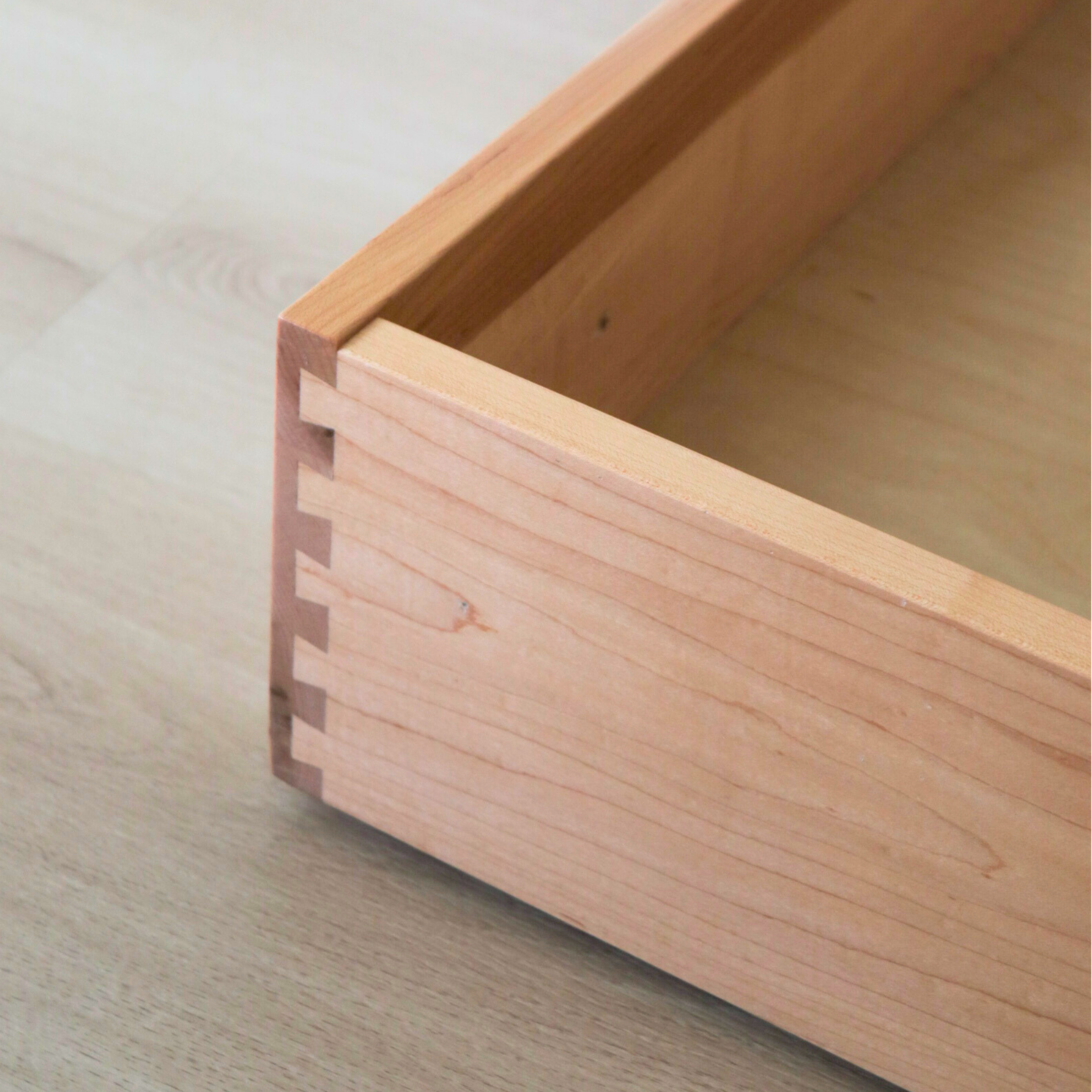 Close-up of a wooden box with finger joints on the corner, sitting on a light-colored wooden surface.