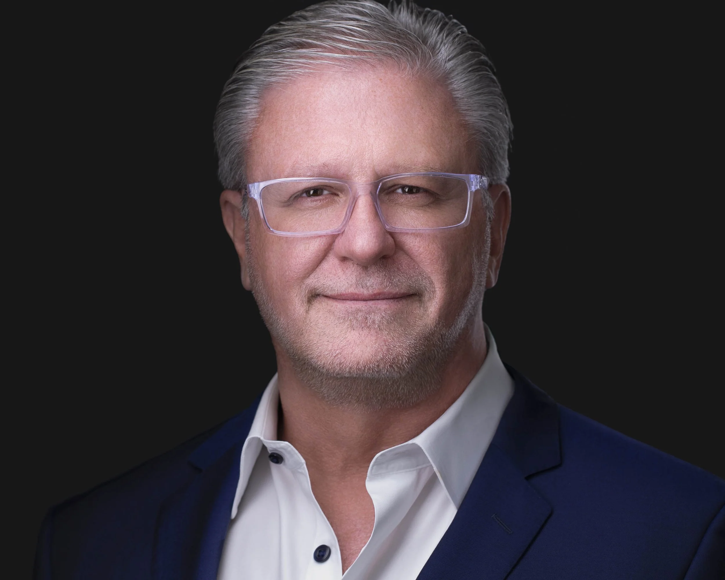 A sharp, distinguished executive headshot taken at Godoy Shots Studio in Dallas, TX. The dark background and tailored suit convey authority and credibility, while the clear, confident gaze adds a personable touch. Ideal for business leaders, board me