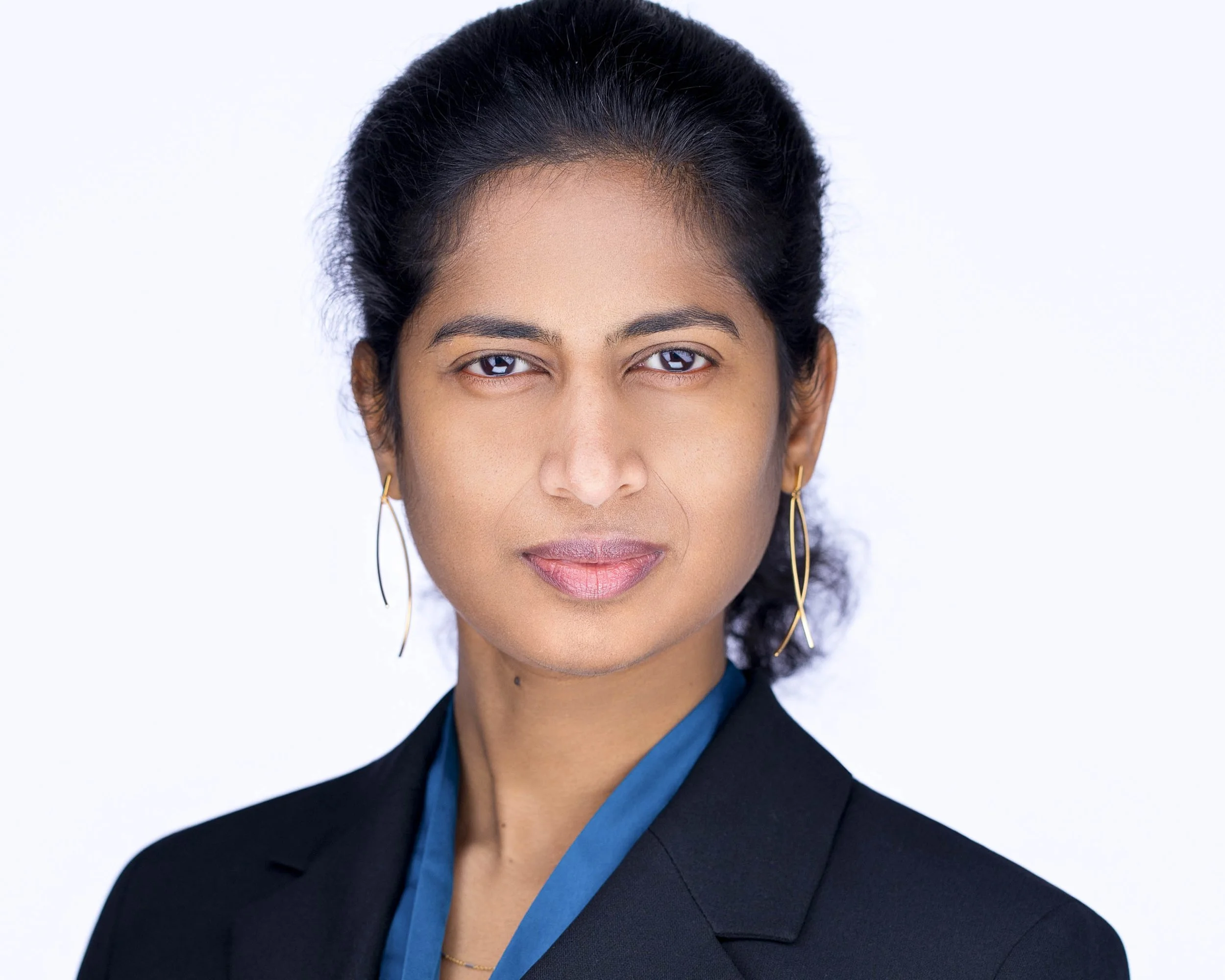Woman with her hair pulled back wearing a dark blazer and blue blouse against a white background.