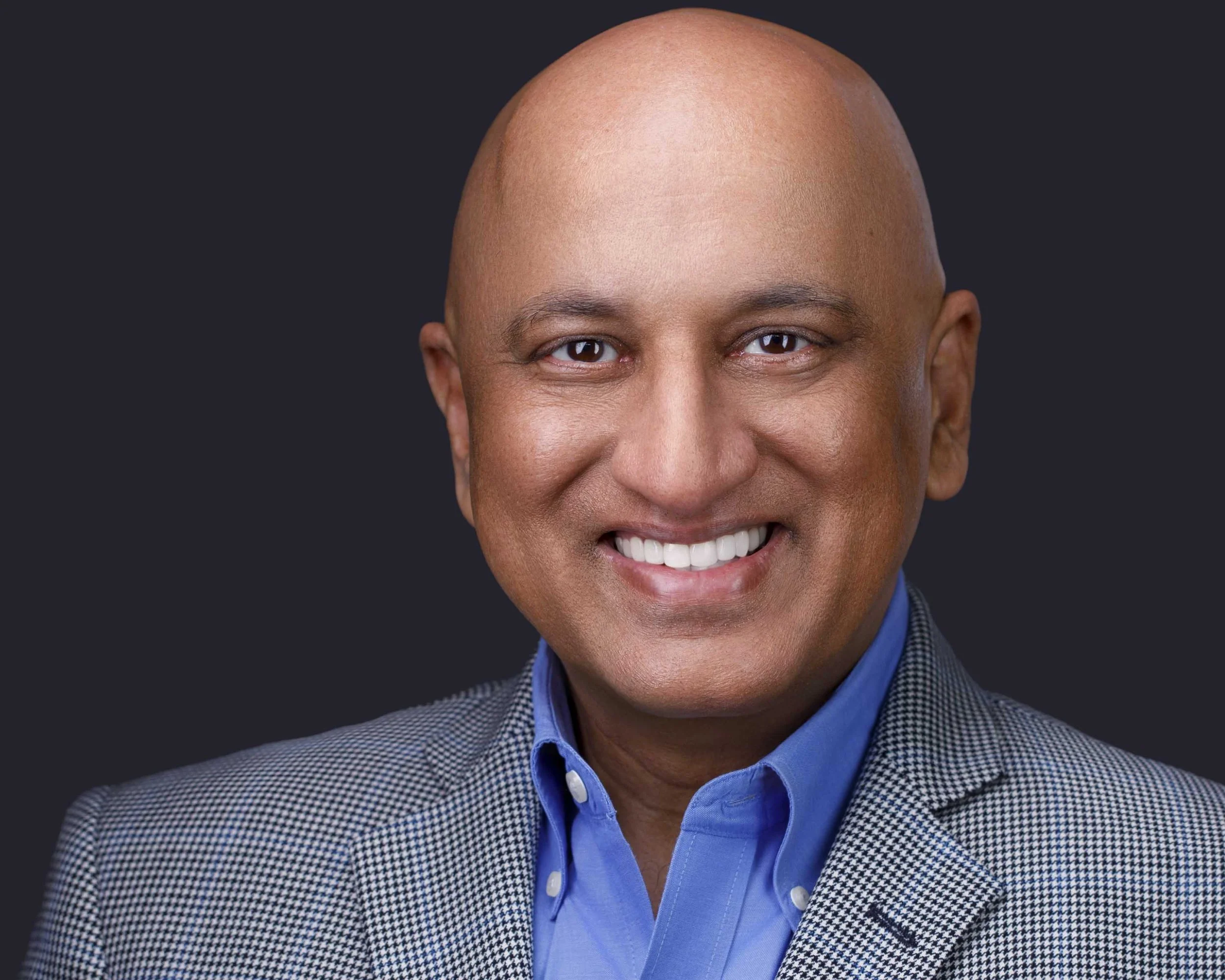 Professional headshots Dallas TX – business headshot of man in blue shirt and checkered blazer, smiling warmly in Dallas professional headshot studio with clean background.
