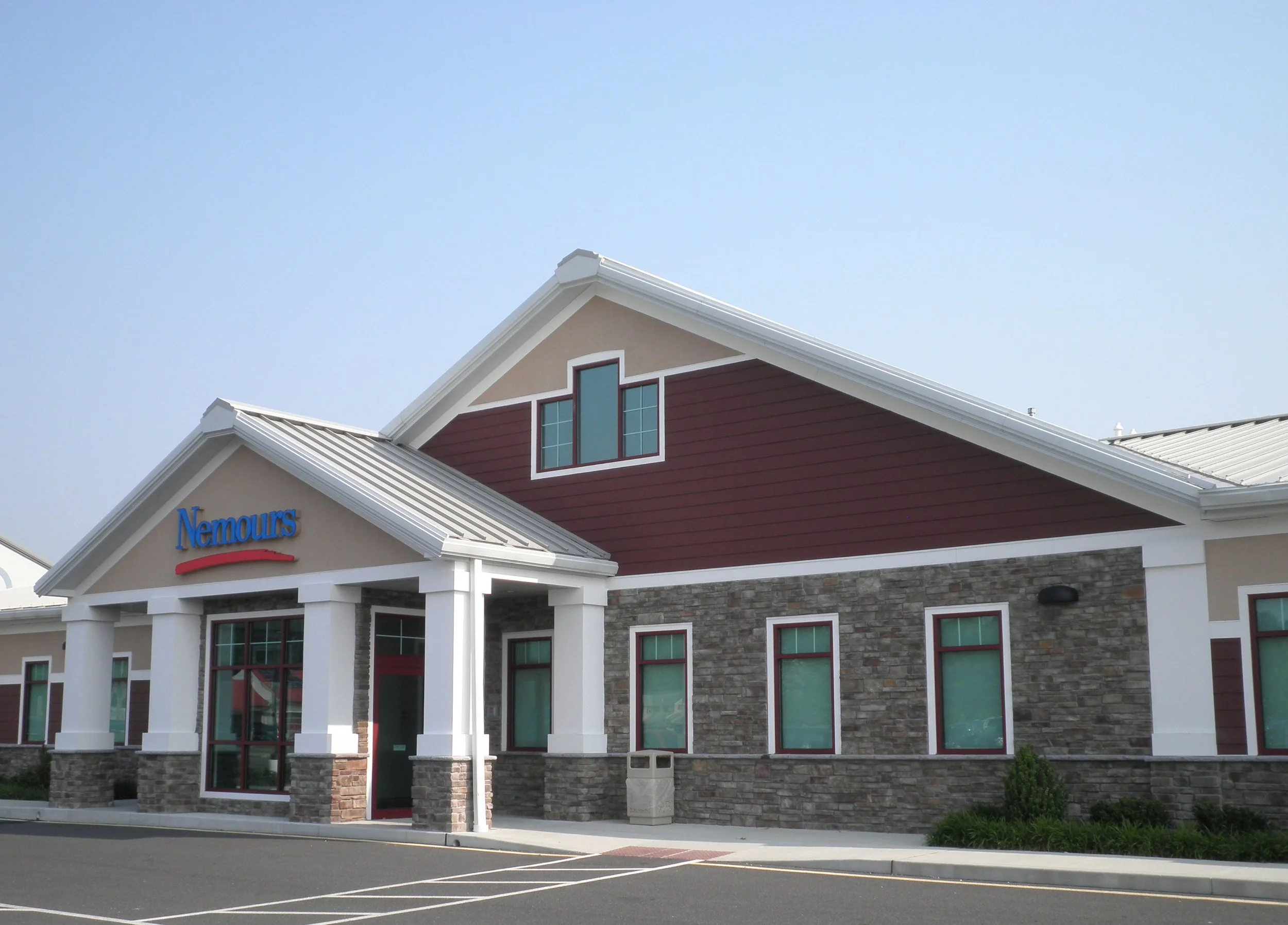 Exterior of a Nemours building with stone and siding facade, multiple windows, and a parking lot in front.