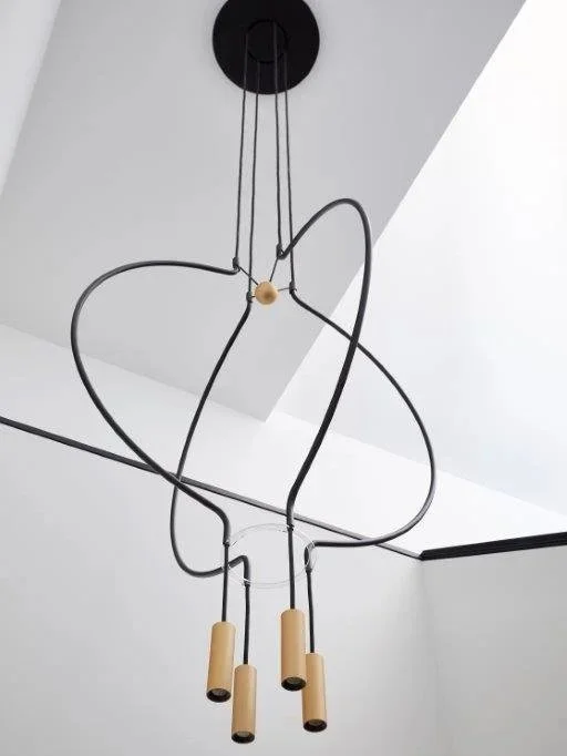 Modern pendant light fixture with black metal loops and wooden accents hanging from a black ceiling mount.