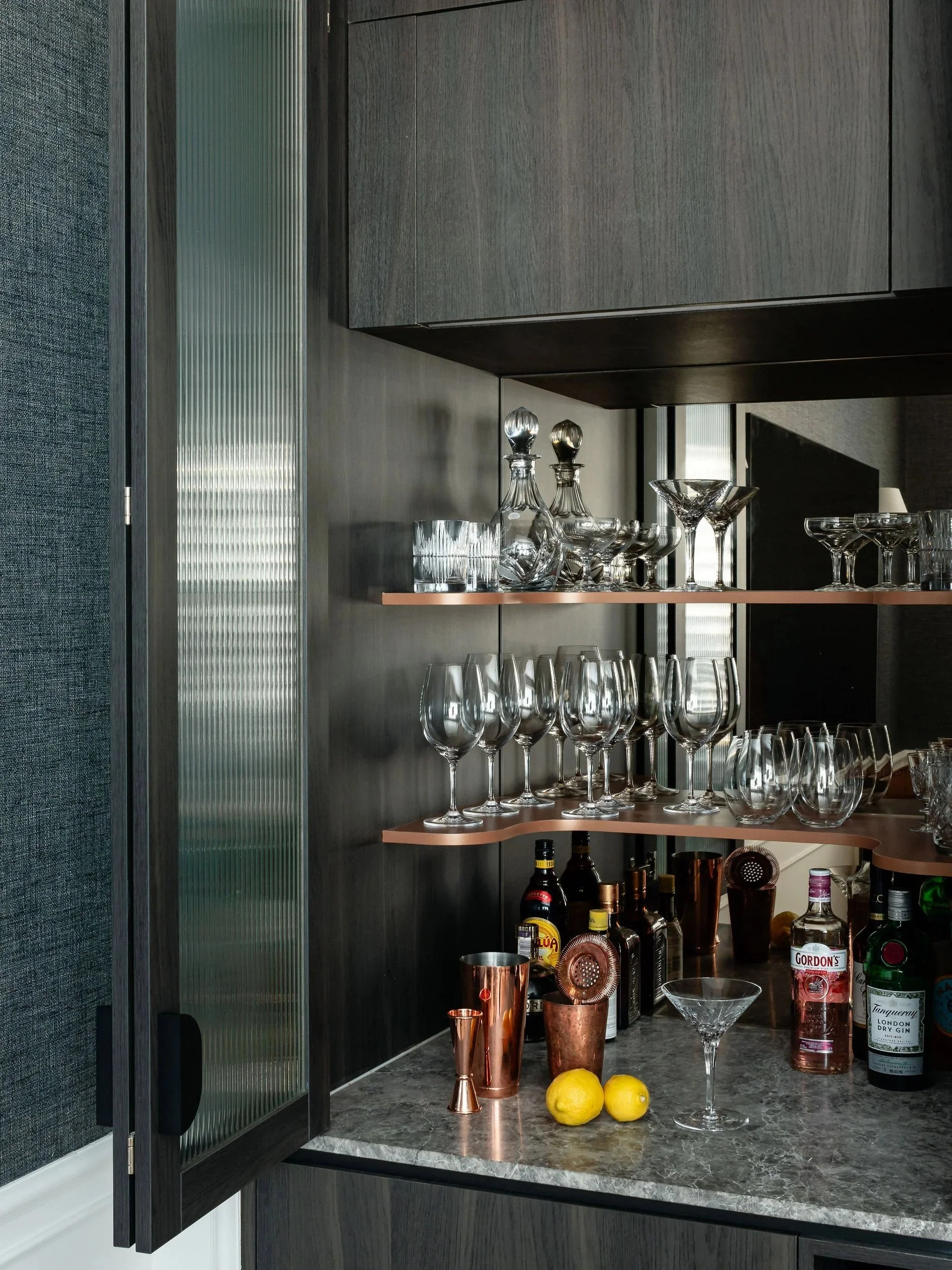 A bar cabinet with glassware, liquor bottles, and bar accessories on shelves and countertop.