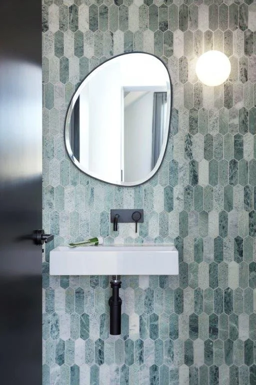 Small bathroom with hexagon patterned tile wall, oval mirror, white rectangular sink, and round wall light
