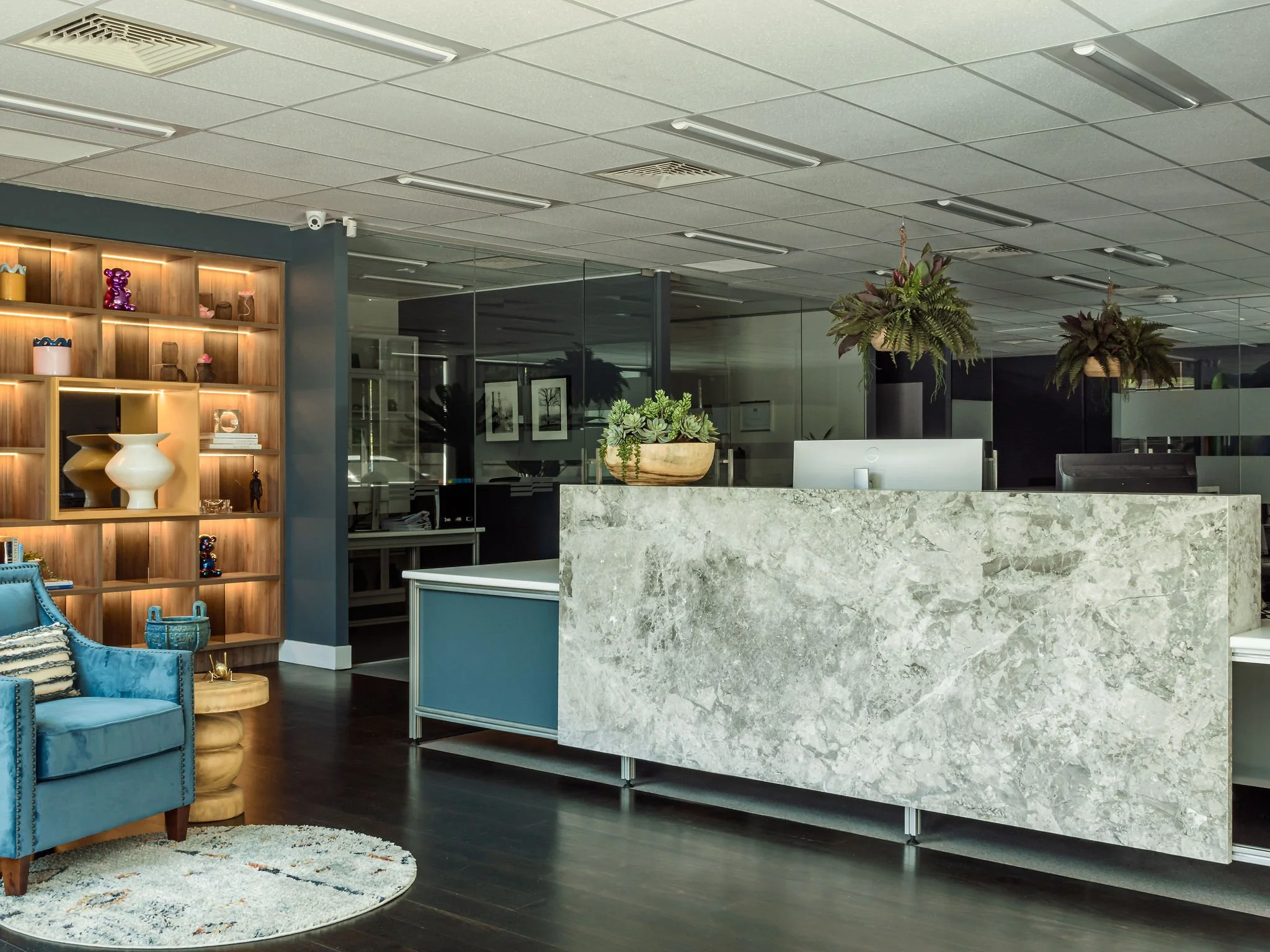 Modern office reception area with marble desk, decorative plants, and shelving with decorative items