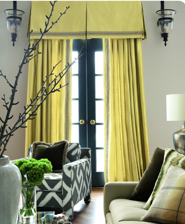 A bright living room with yellow curtains covering a glass door, black and white patterned armchair, beige sofa with pillows, and decorative lighting fixtures on walls.