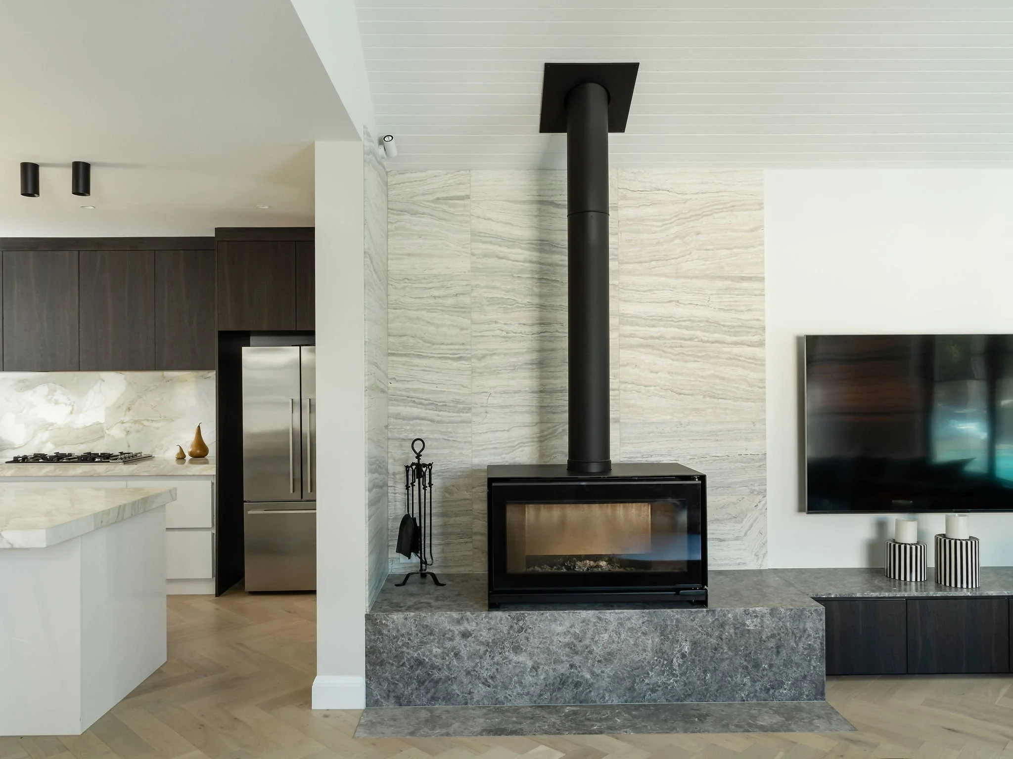 Modern living room with a fireplace, flat-screen TV, dark wood cabinetry, and a marble backsplash in the kitchen.