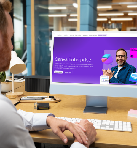 Person working on a desktop computer displaying Canva Enterprise webpage with a smiling man and colorful graphics.