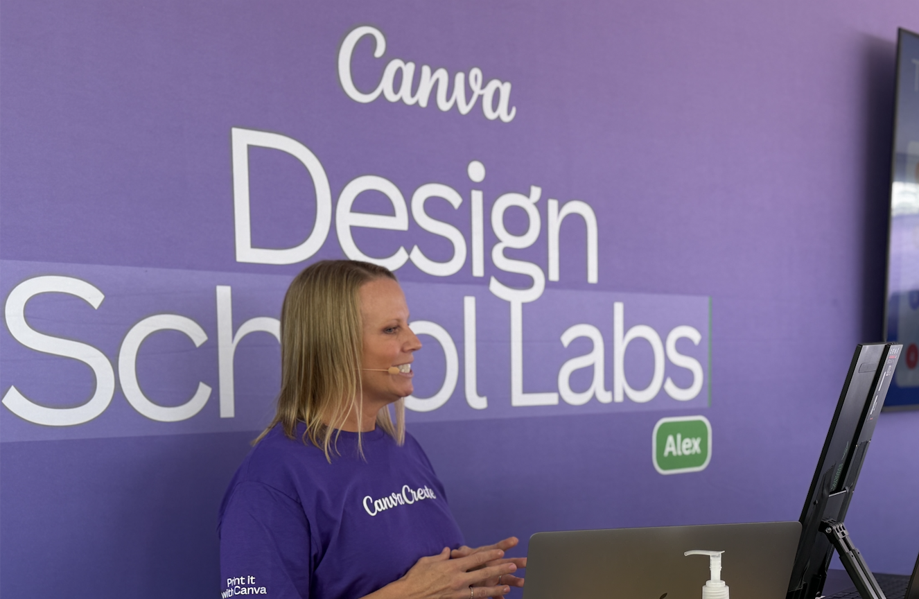 Rebecca Flint, Canva Expert, Woman with blond hair speaking at a presentation on Canva Design School Labs, wearing a purple shirt that says 'CanvaCreate' and sitting in front of a large screen with the words 'Canva Design School Labs'.