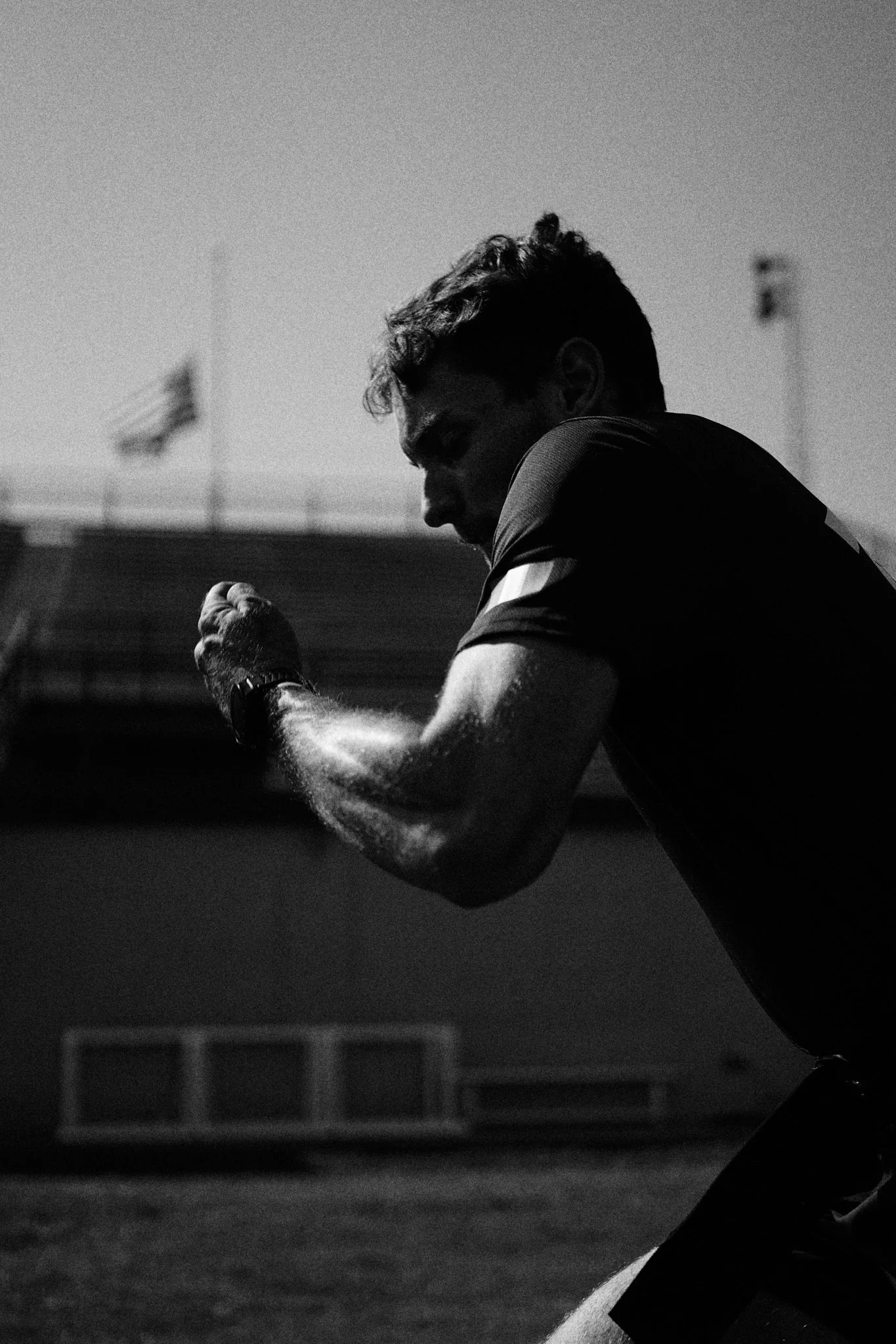 A man in athletic clothing doing a workout or practice at a sports field, with American flags in the background.