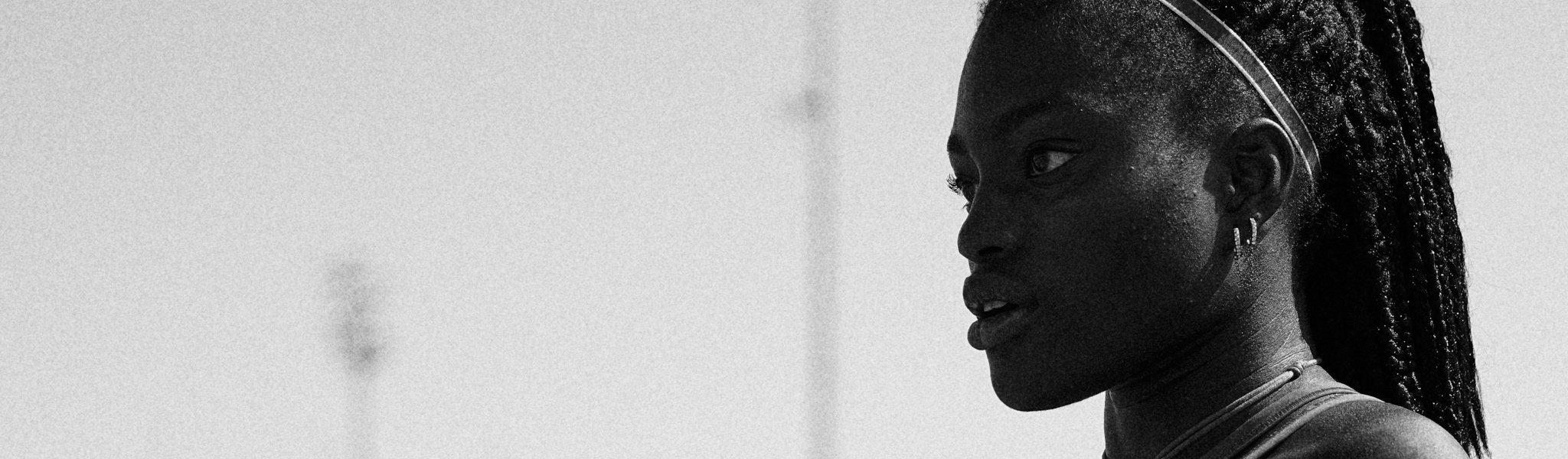 Close-up of a woman's face in profile with textured skin and braided hair, wearing earrings and jewelry, in black and white.