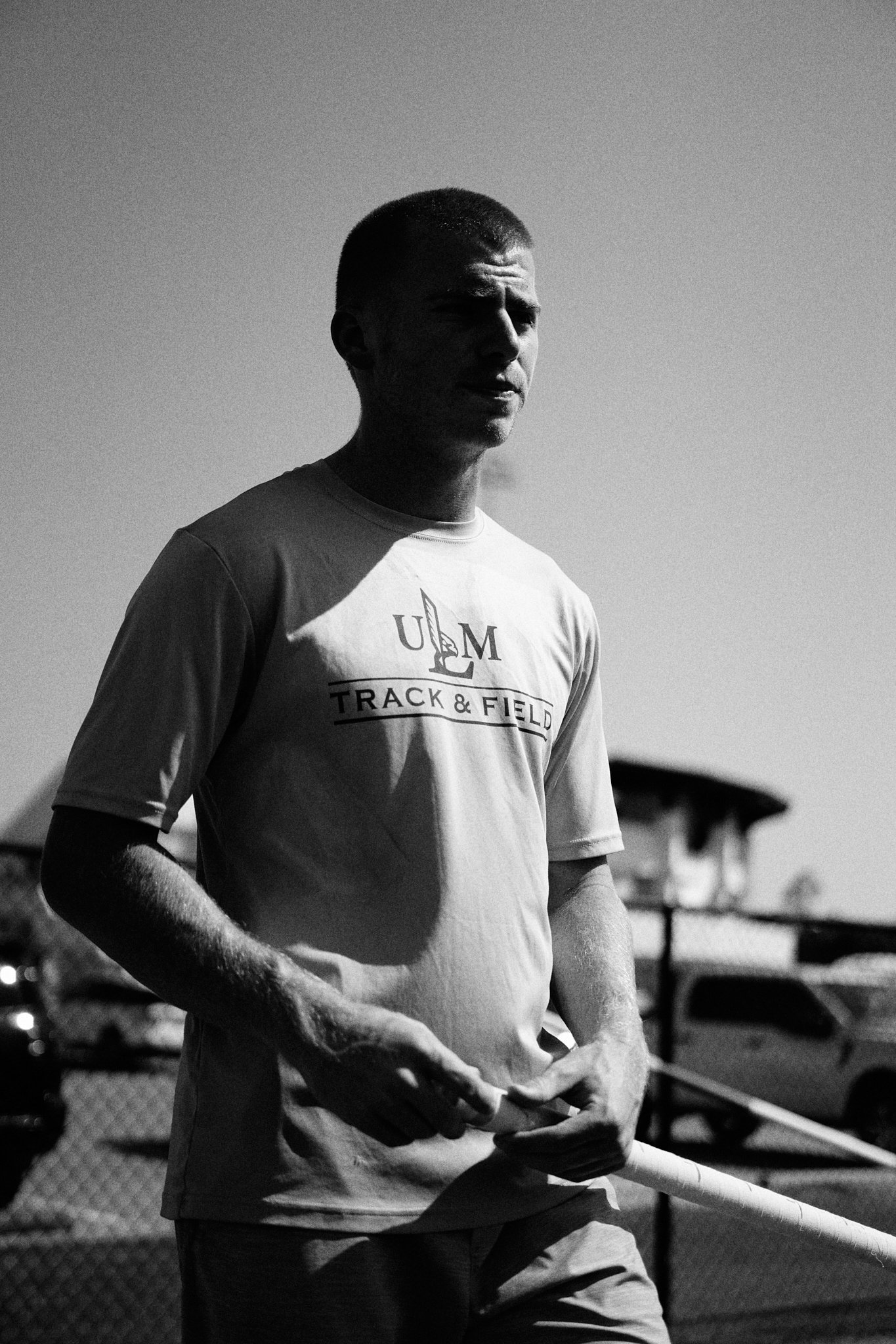 A young man holding a discus, wearing a T-shirt with 'U.M. Track & Field' on it, standing outdoors in daylight.