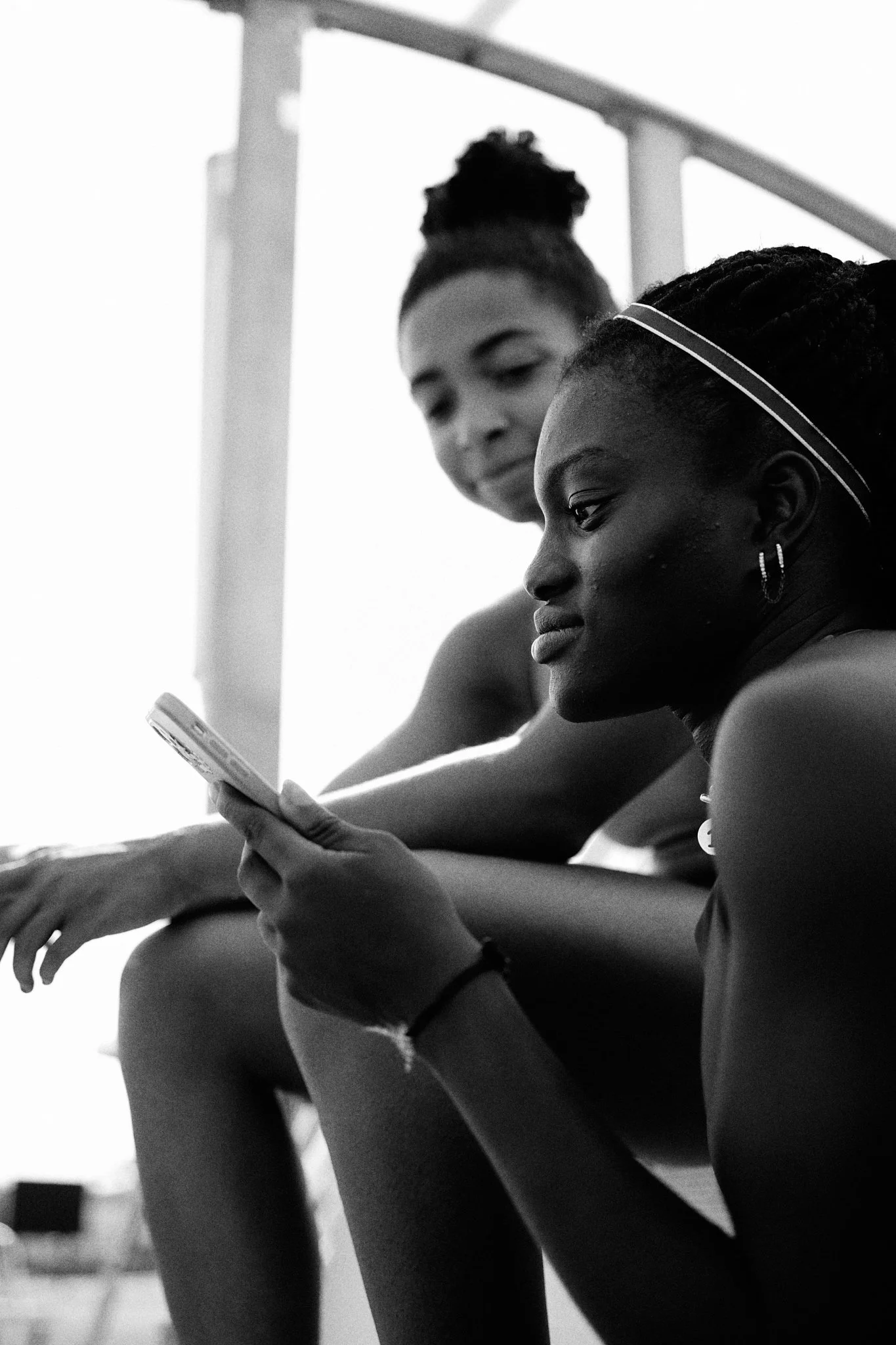 Two young women sitting on stairs, one is looking at her phone, both are relaxed.