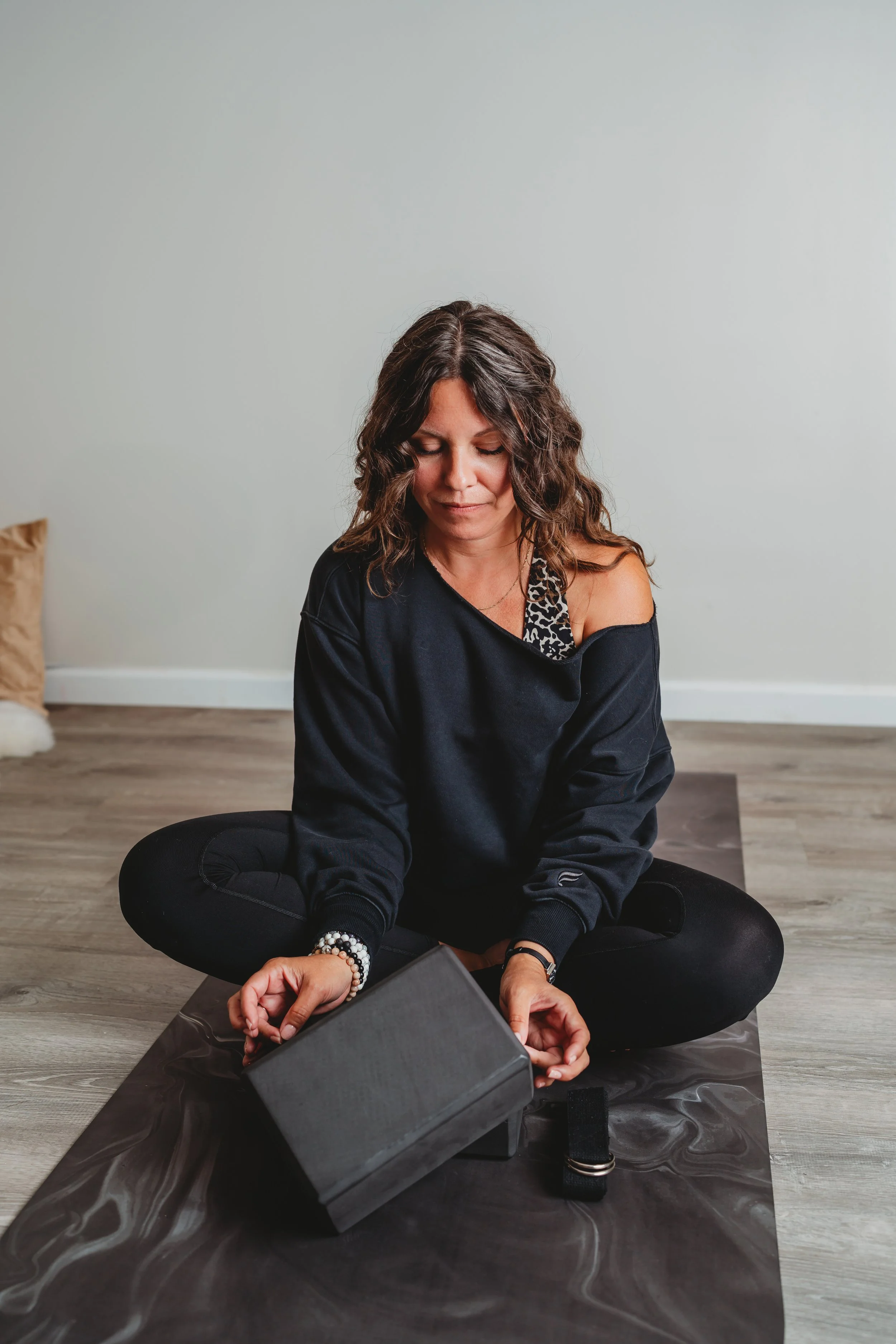 Woman sitting cross-legged on a yoga mat with eyes closed, practicing meditation indoors.