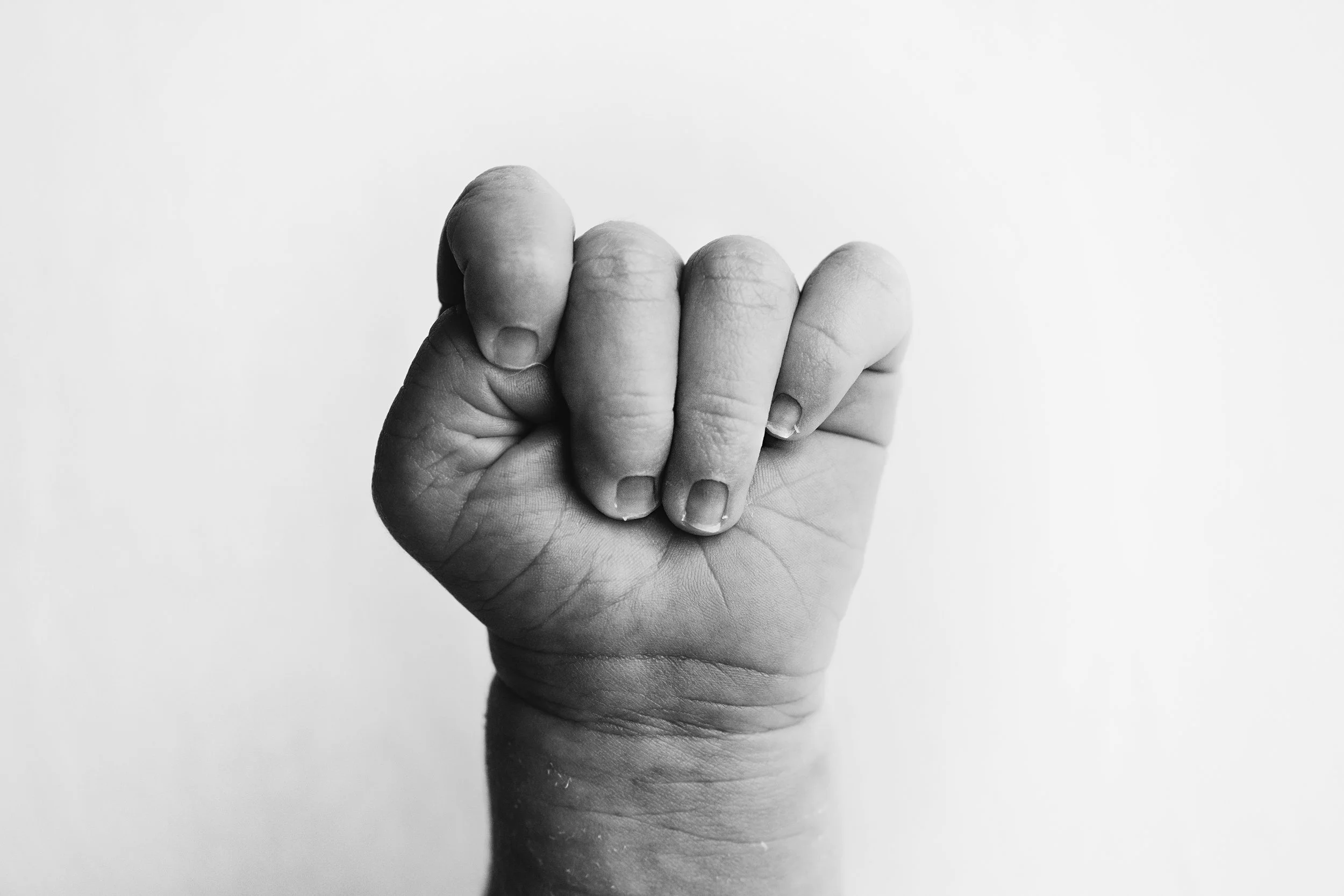 A black and white photo of a clenched fist with the fingers curled into the palm, viewed in front of a plain background.