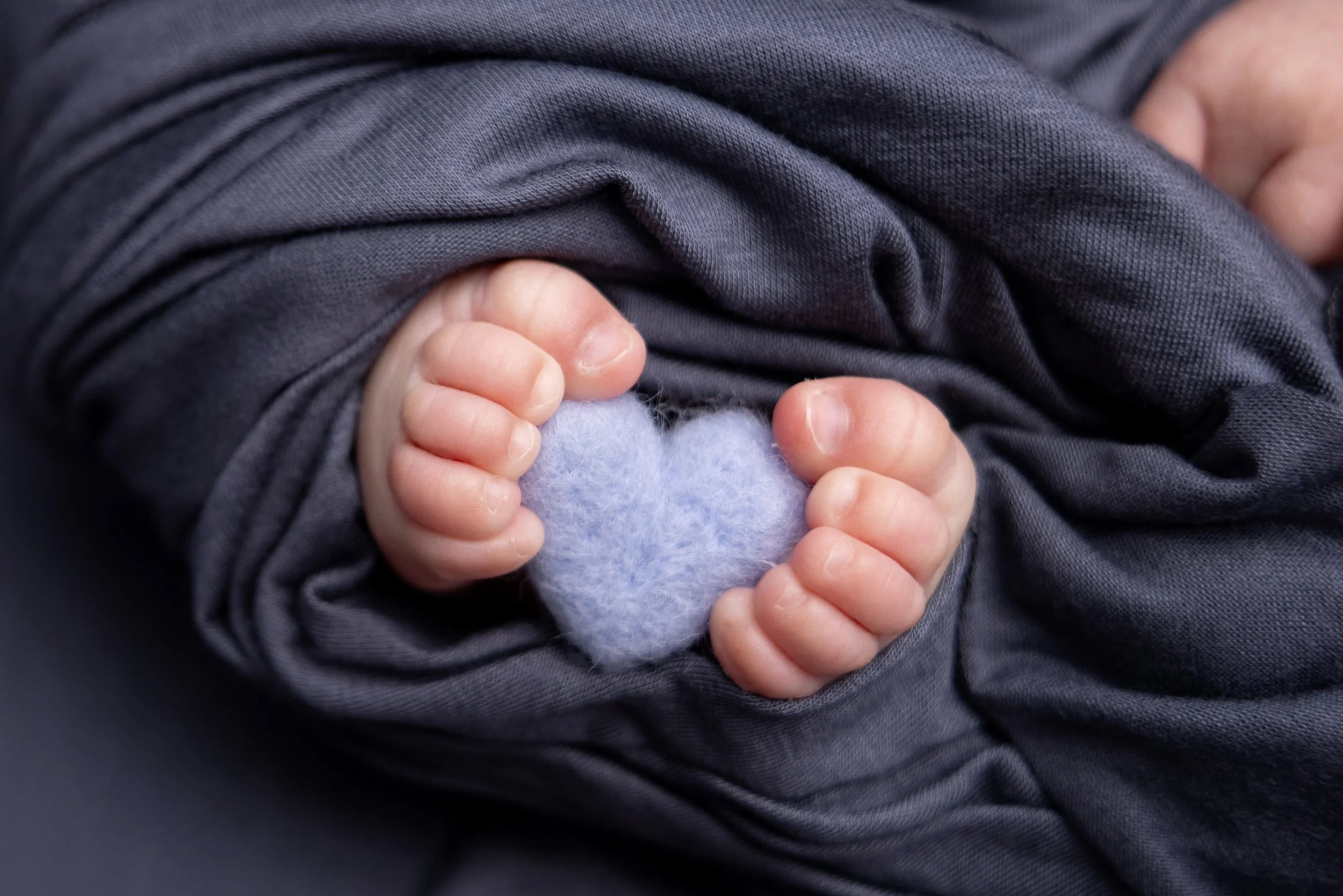 Close-up of a baby's hand holding a small, light purple, heart-shaped object.