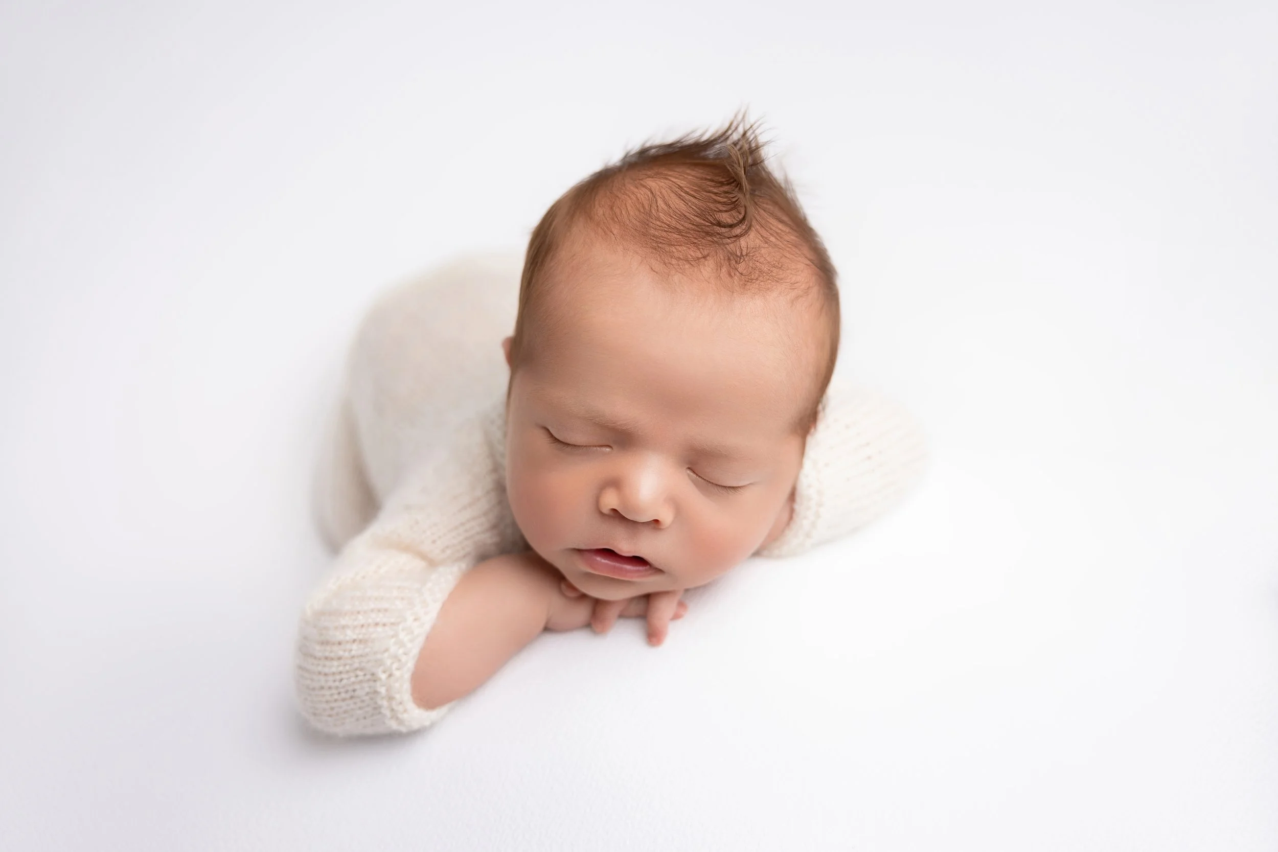 Close-up of a sleeping newborn baby with a knitted cream sweater and a white background.