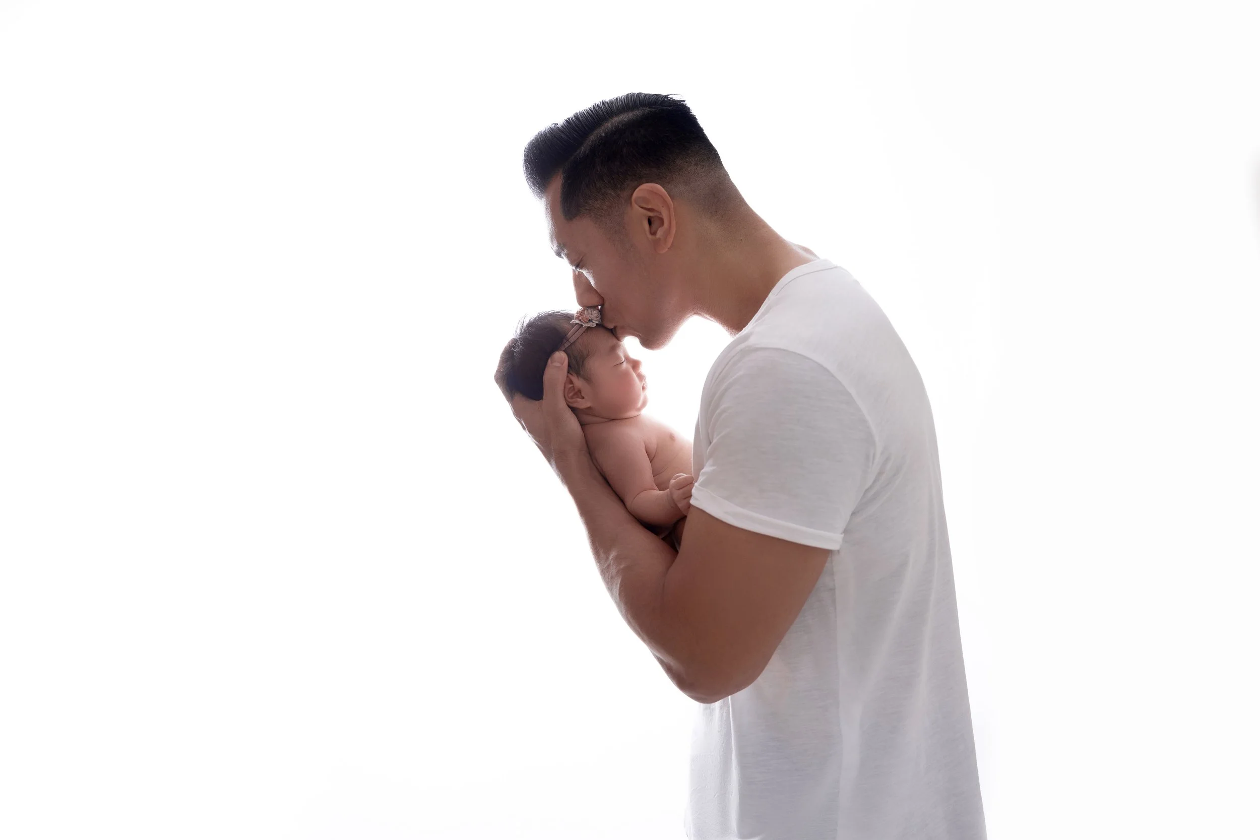 A man holding a newborn baby close, touching foreheads and noses, in front of a white background.