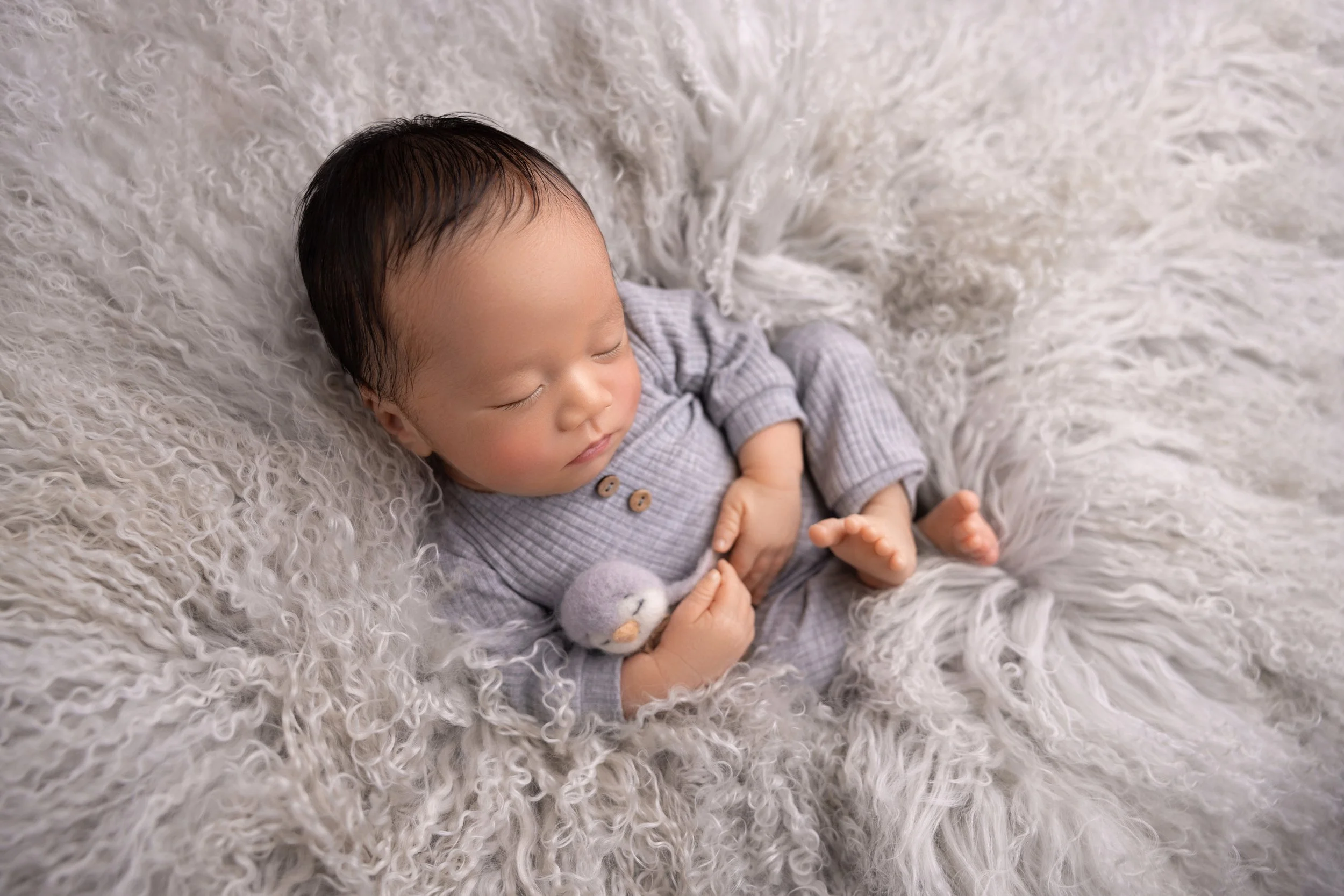 A sleeping baby with dark hair lying on a soft, fluffy white blanket.