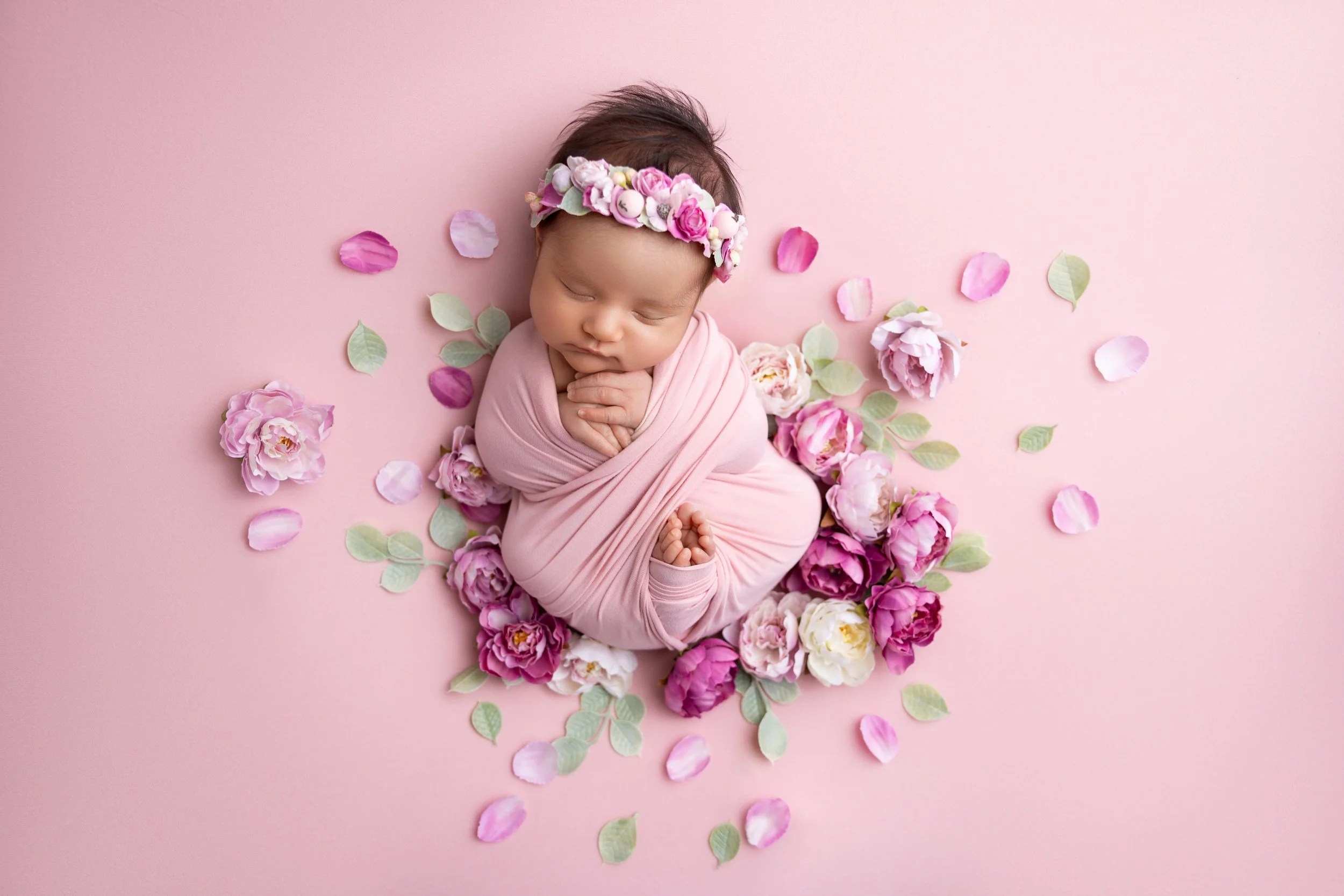Soft and dreamy newborn girl photo session with pink flowers — baby wrapped in blush pink and surrounded by floral accents. Luxury newborn photography in Los Angeles by Grethel Villate.