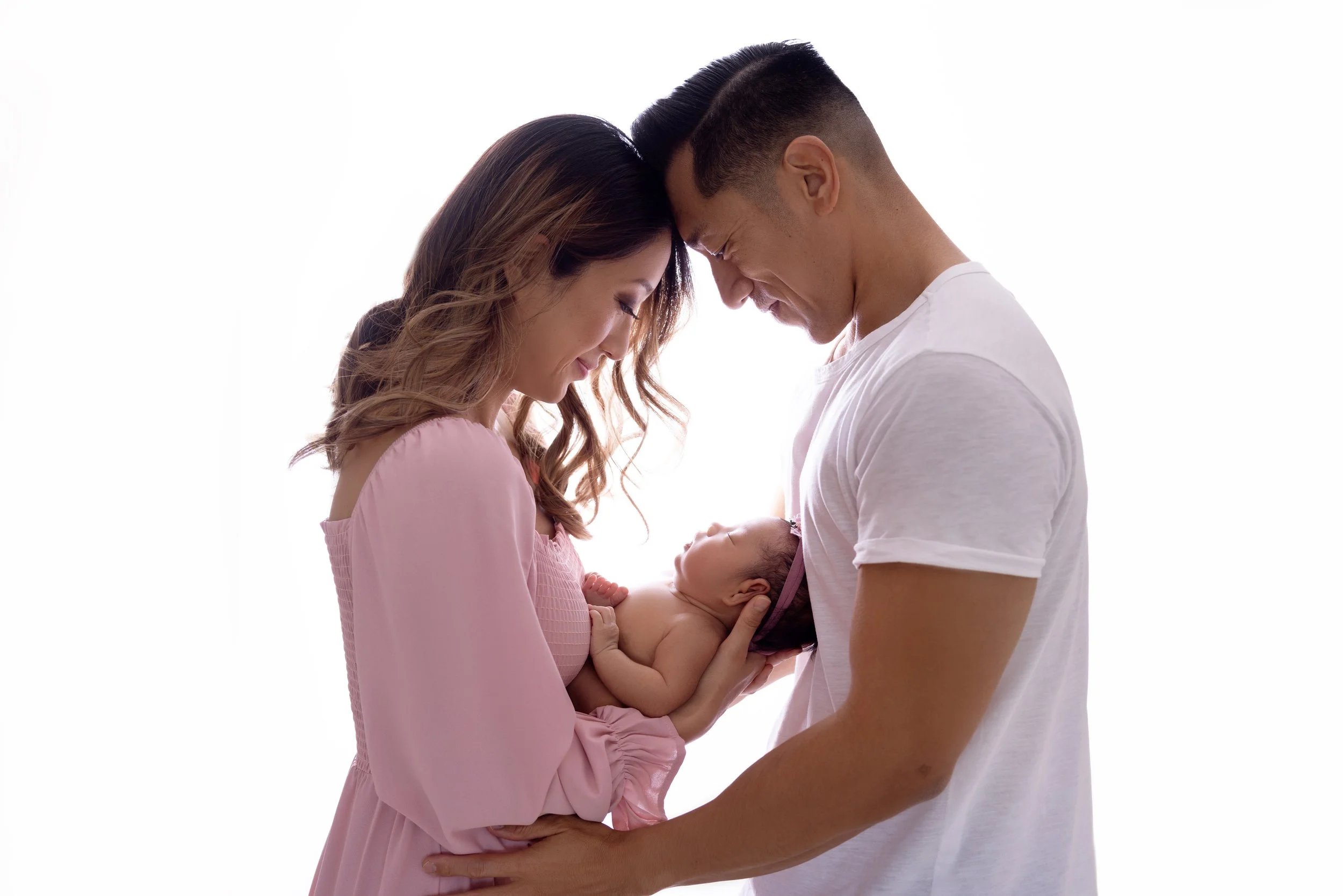 A couple holding and looking at their newborn baby together against a white background.