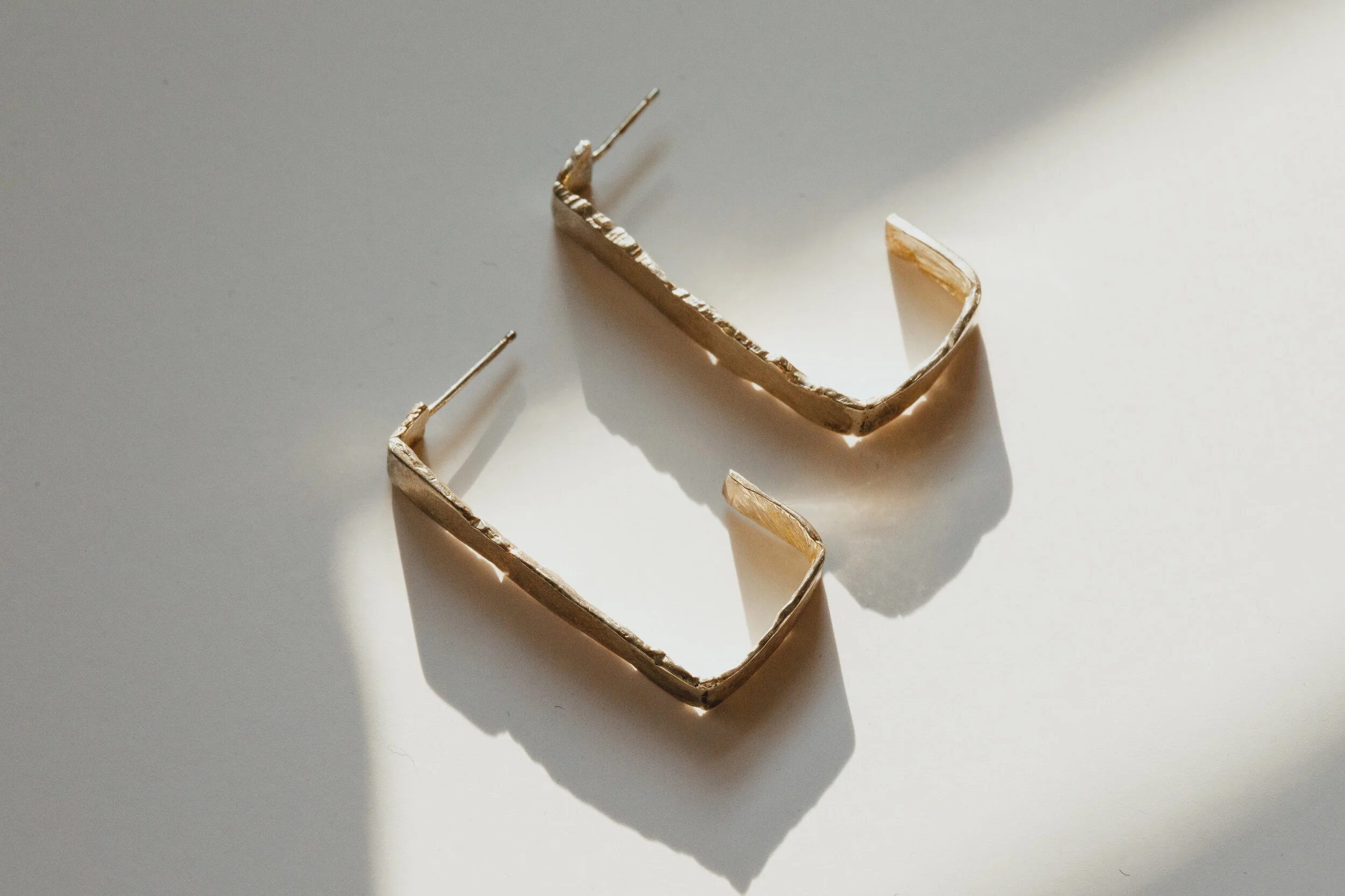 Close-up of a gold hair clip on a white surface, with shadows cast by sunlight.