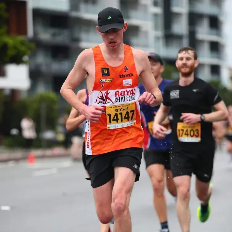 A group of runners participating in a marathon on an urban street, with buildings in the background, wearing athletic gear and race bibs.