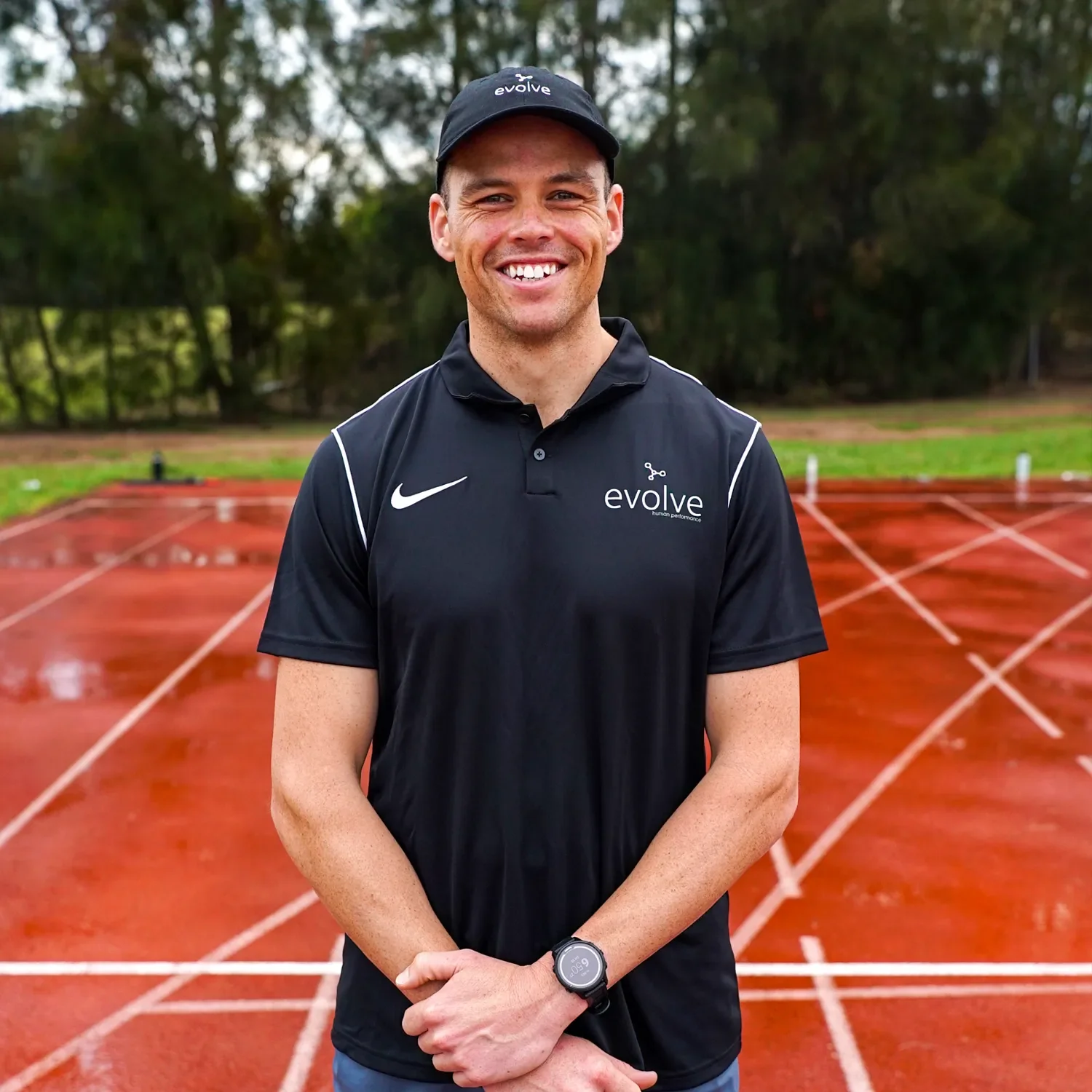 Man standing in front of running track wearing an evolve polo shirt