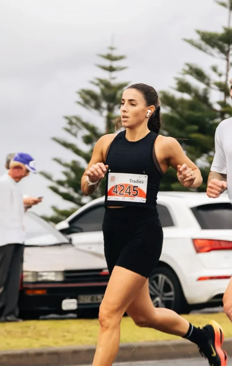 Female marathon runner in black athletic attire running outdoors during daytime, wearing earphones and a race bib numbered 4245.