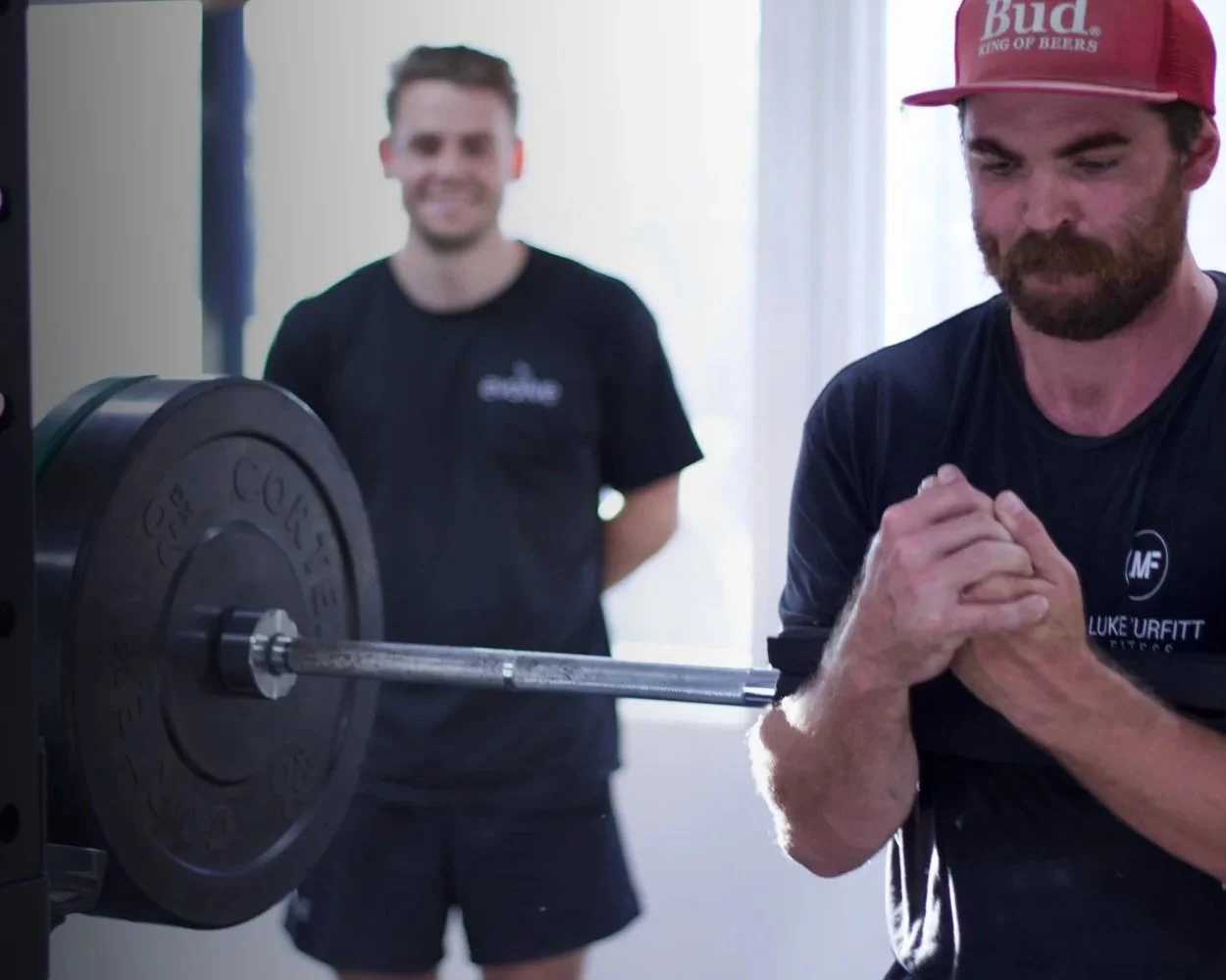 Personal trainer coaching a small group training session with man lifting barbell