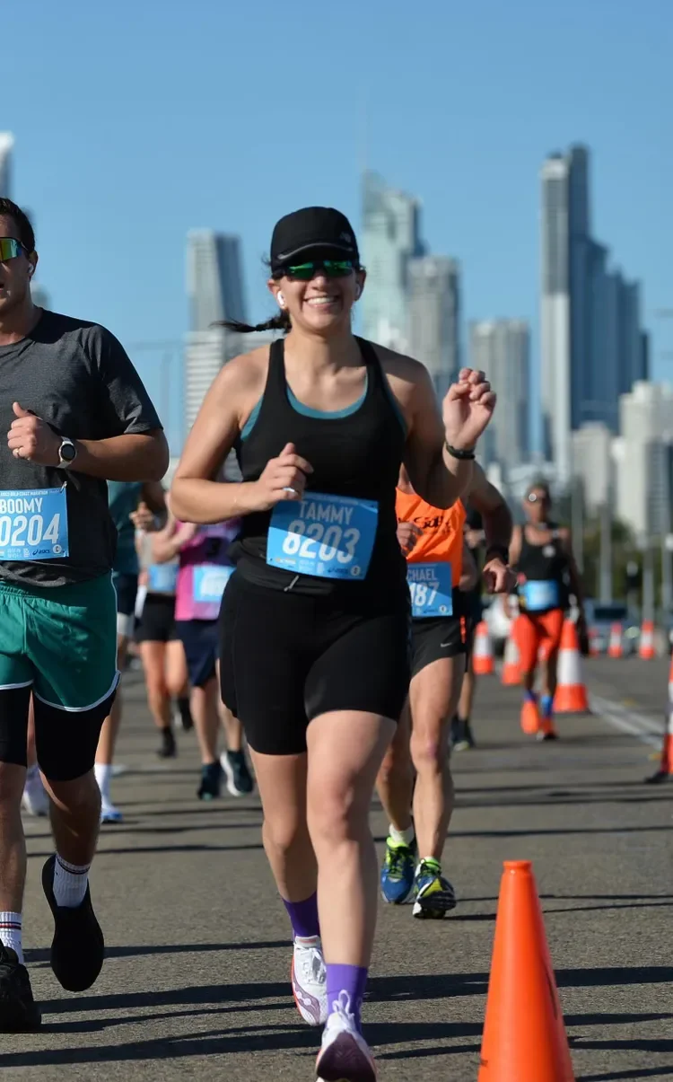 Group of runners participating in a marathon, with a city skyline in the background, marked with orange traffic cones.