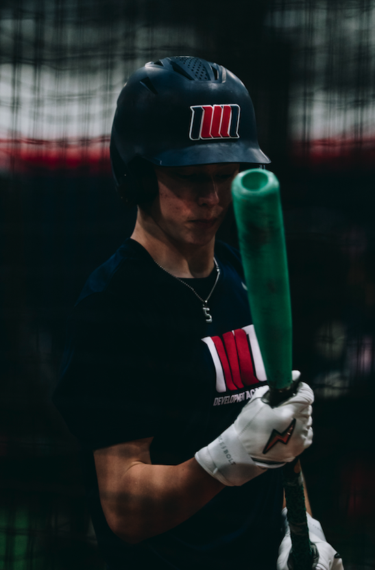 Academy hitter in a Northwest Nationals helmet holding a green training bat