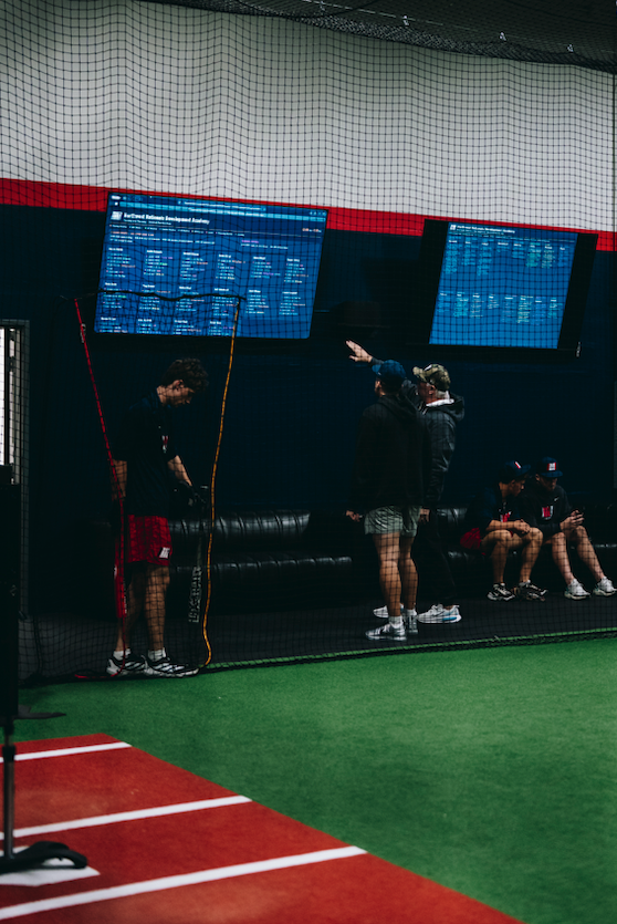 Players gathered by data screens at the Northwest Nationals indoor baseball facility