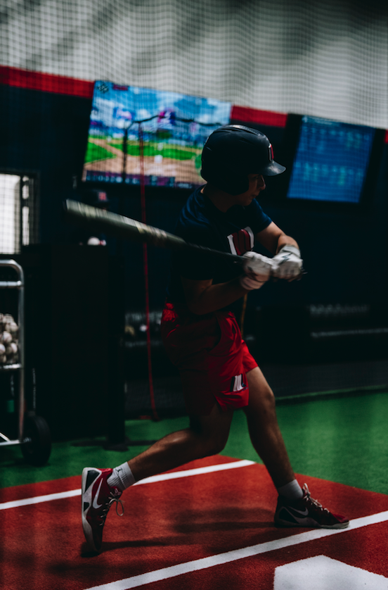 Hitter swinging in an indoor cage with screens behind at Northwest Nationals