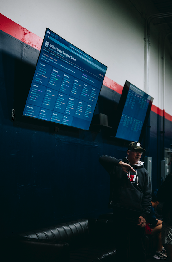 Coach standing below wall mounted data screens at Northwest Nationals Development Academy