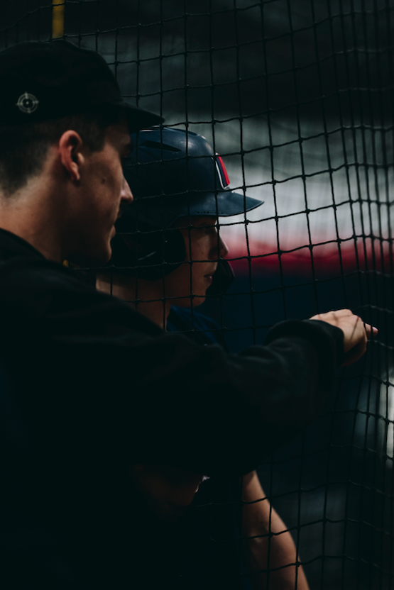 Coach and helmeted hitter talking at the batting cage net