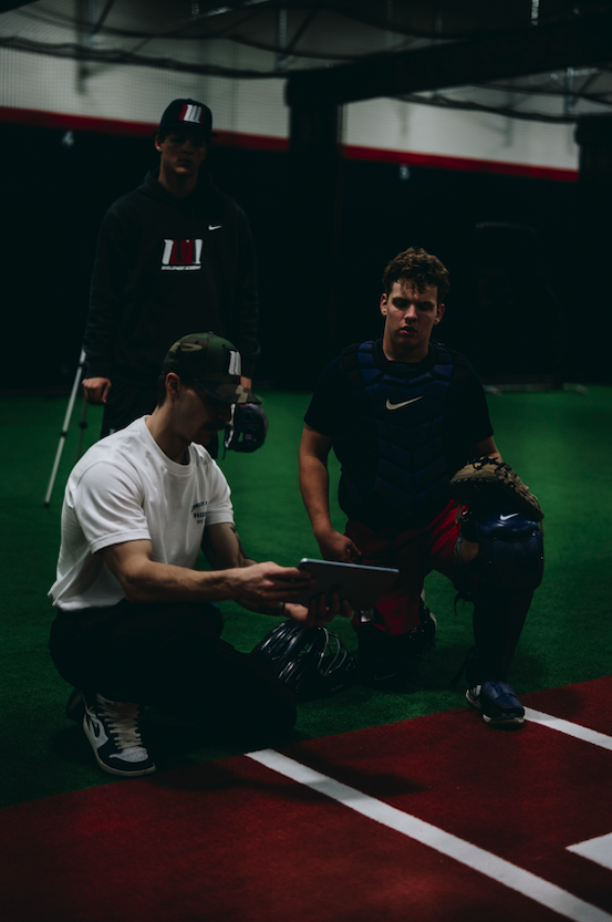 Coach reviewing a tablet with a catcher at Northwest Nationals Development Academy