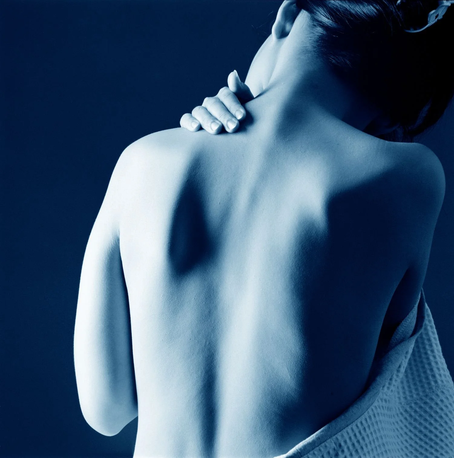 Bodytune Massage stock photo. A person with a short hairstyle touching their shoulder with one hand; the person is wearing a white karate uniform and the background is dark.
