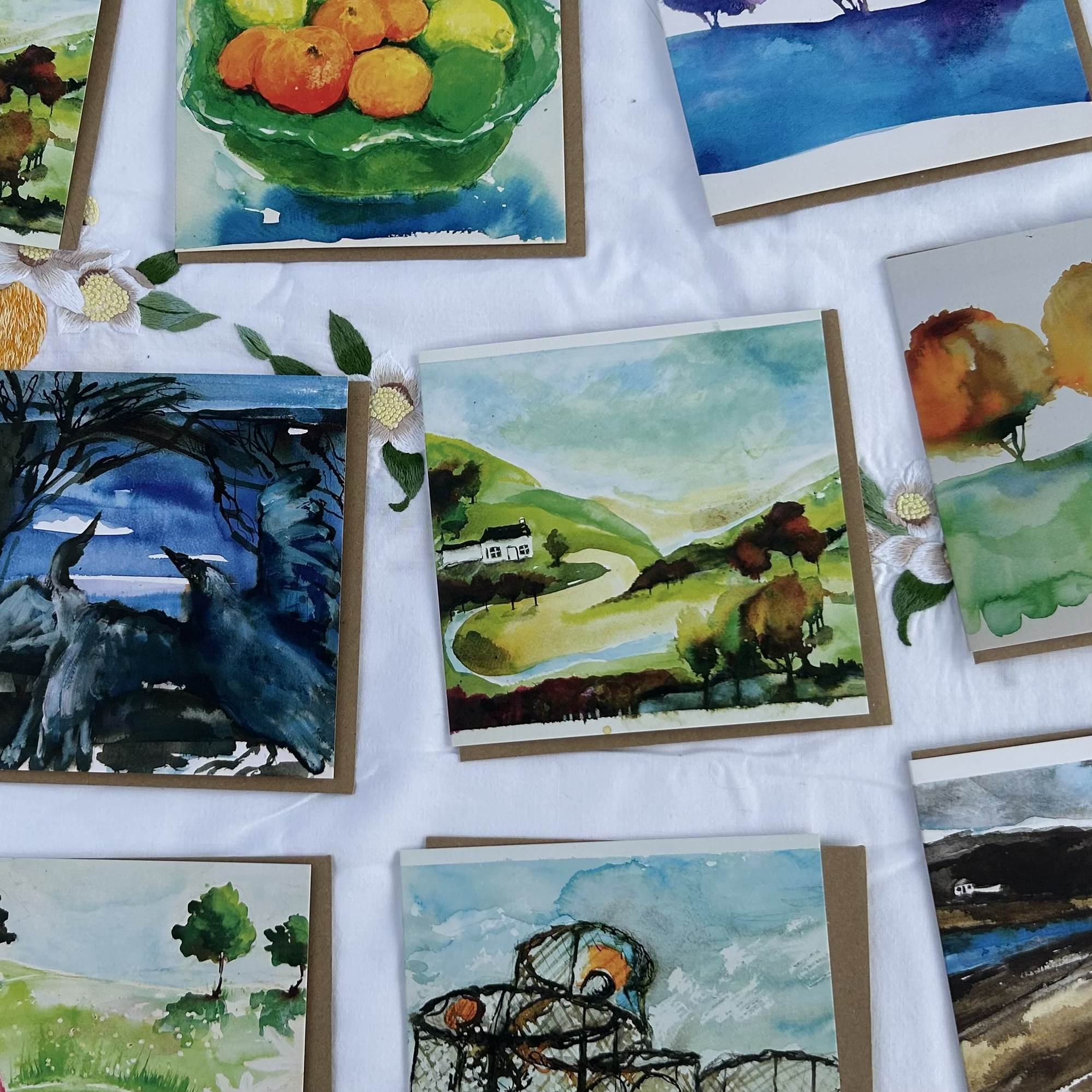 Collection of watercolor paintings depicting landscapes and nature scenes, including countryside hills, trees, a lake, a basket of fruit, and a lake with a building in the background.