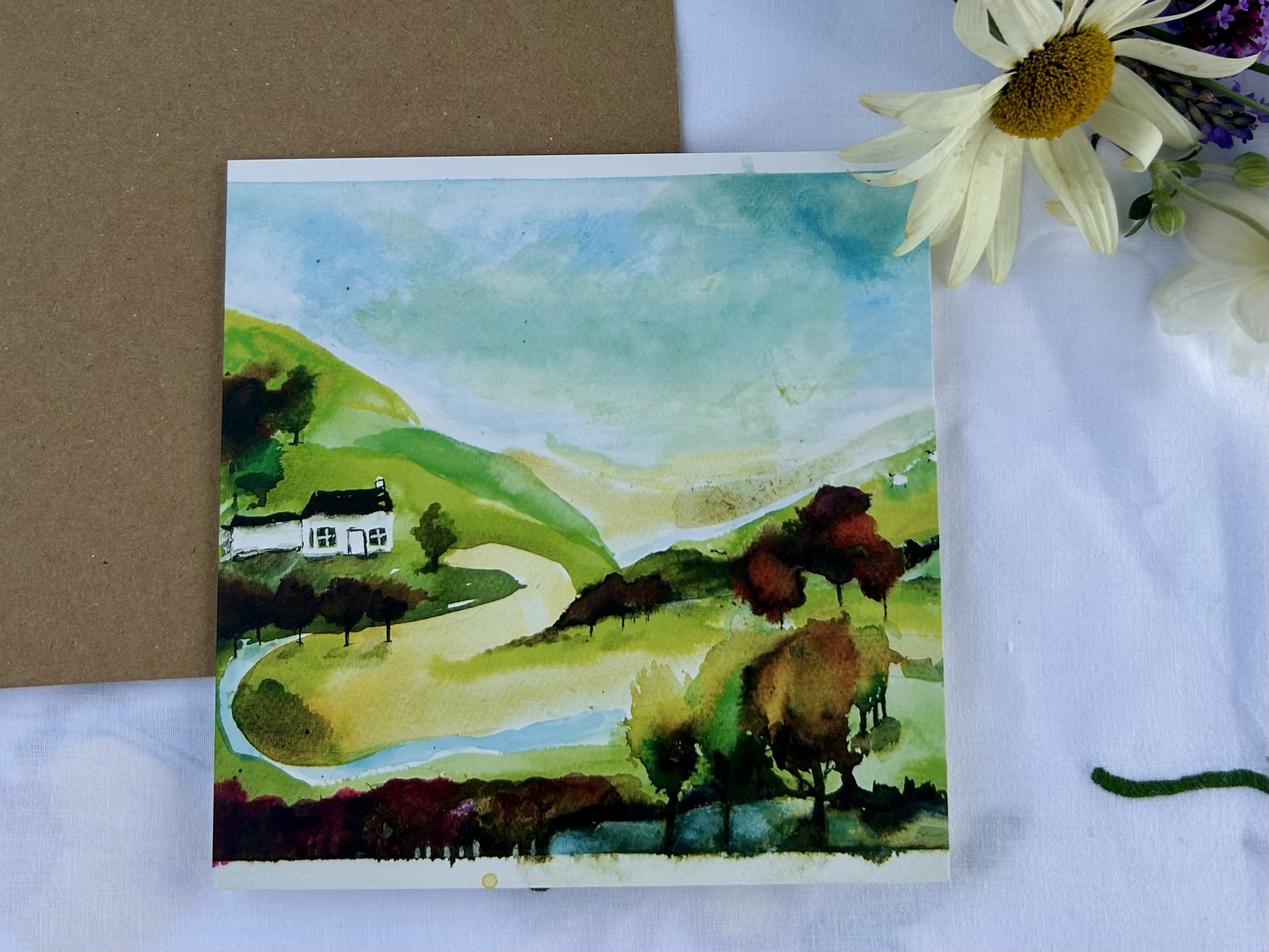 Watercolor painting of a green hillside landscape with a white house, trees, and a winding path, under a partly cloudy sky.