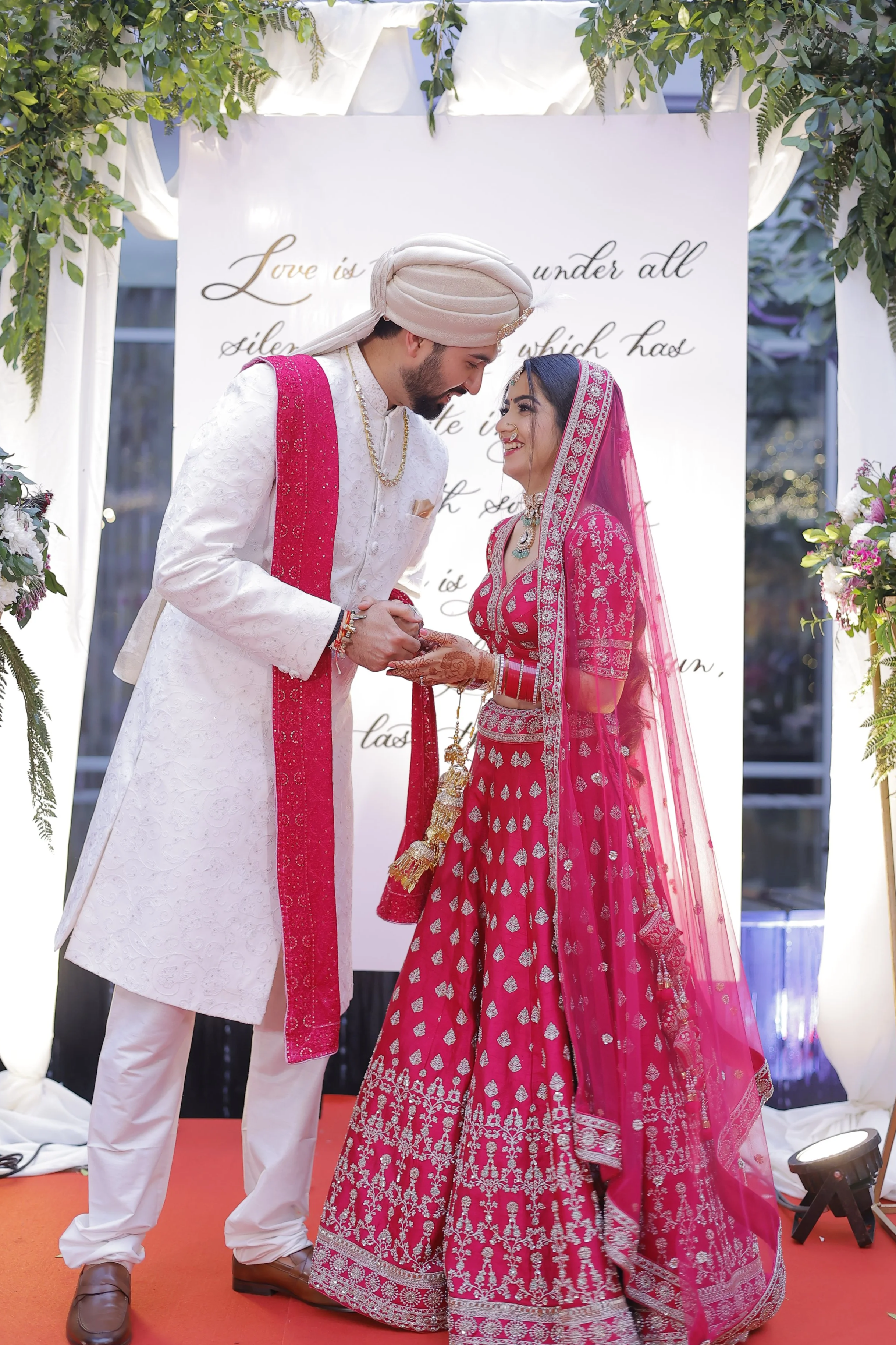 A bespoke hand-lettered calligraphy backdrop for an Indian wedding ceremony with a couple posing in front.