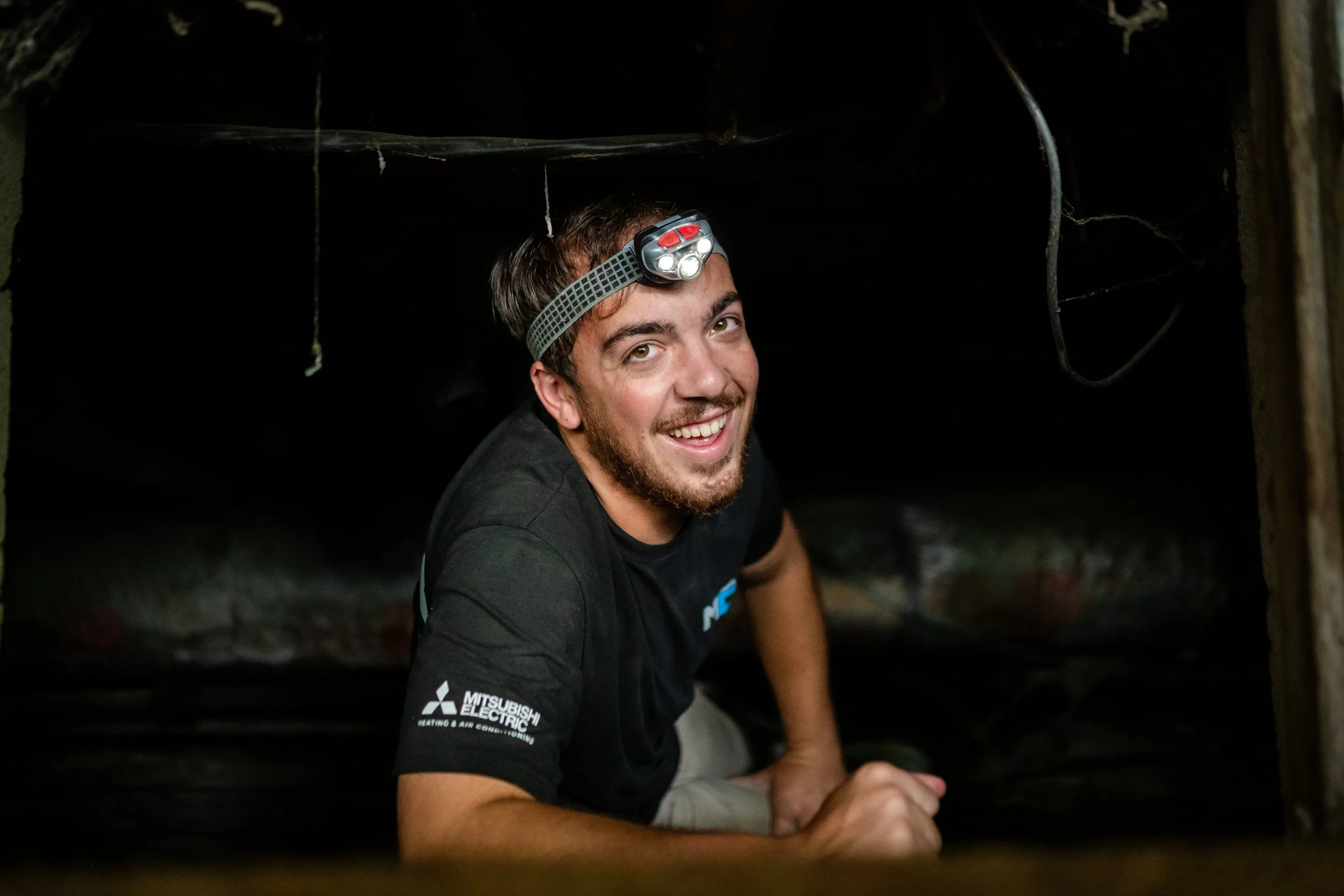 Smiling man with a headlamp crawling in a dark tunnel or underground area.