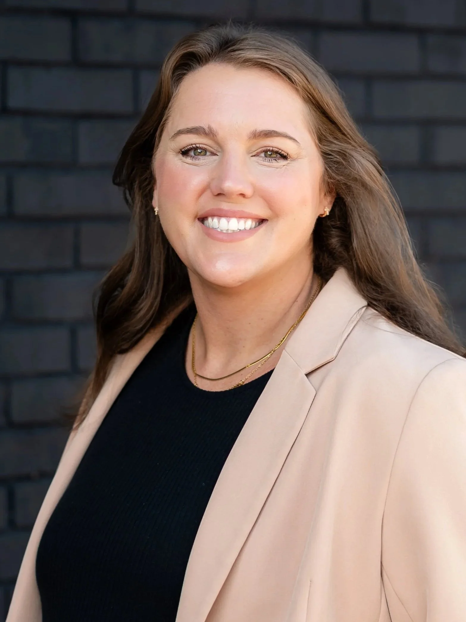 A woman with long curly brown hair holding a few pieces of paper and some kind of card, standing inside a room with guitars on the wall behind her.