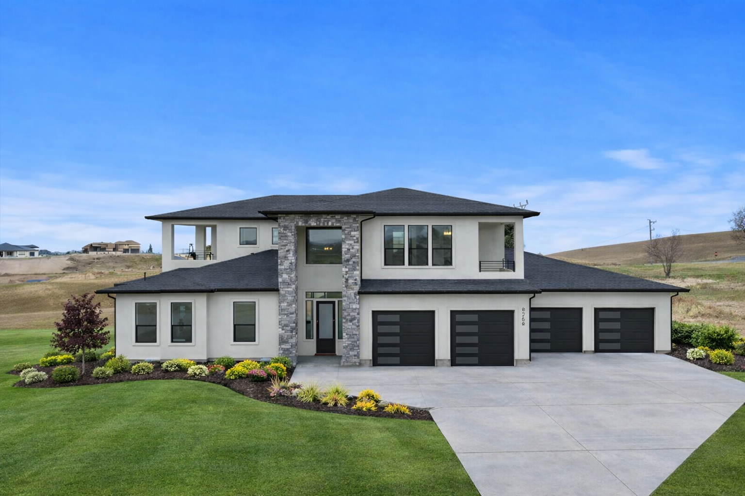 Modern house exterior with stone and wood finishes, large glass windows, potted plants near the entrance, concrete walkway, and gravel landscaping under a partly cloudy sky.