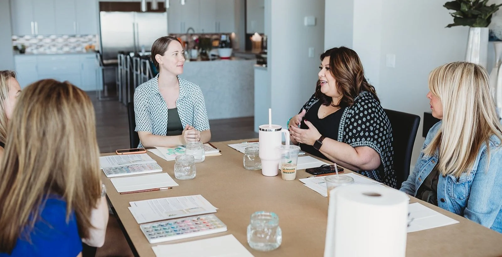 Group of women having a meeting at a conference table in a modern office kitchen.