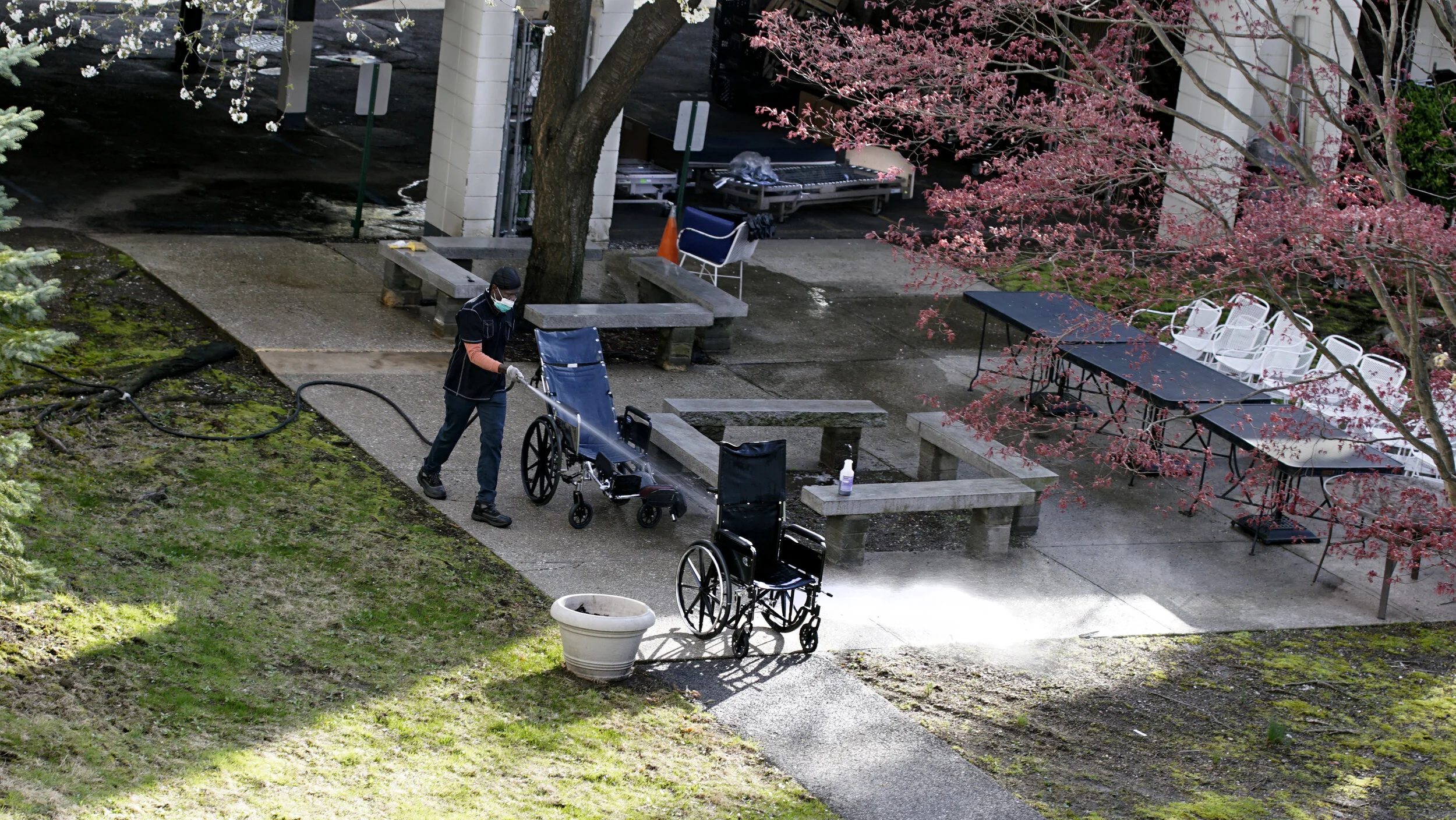 Healthcare worker hosing down the wheelchair outside a nursing home.